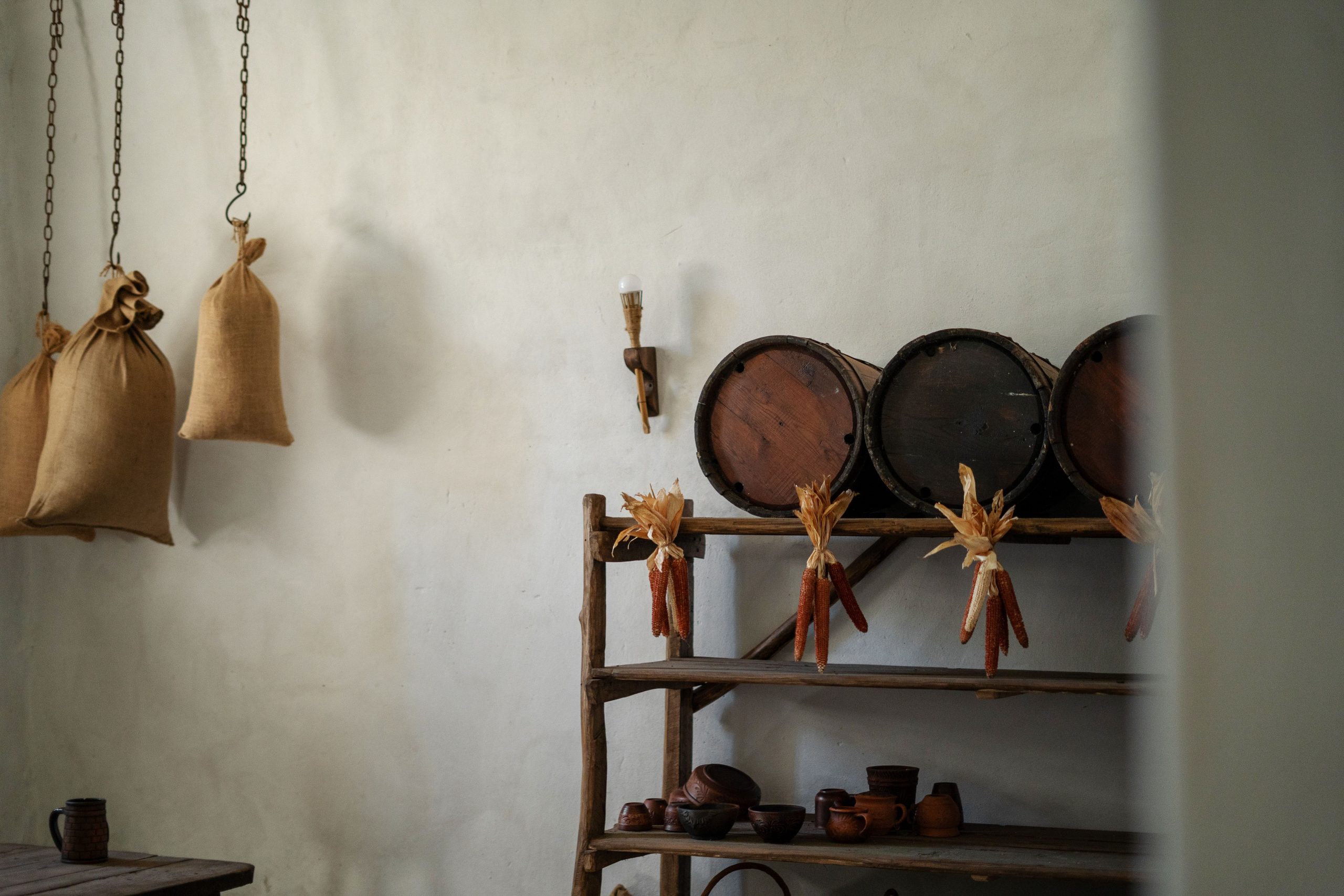A rustic kitchen interior featuring hanging burlap sacks and wooden shelves with dried corn.
