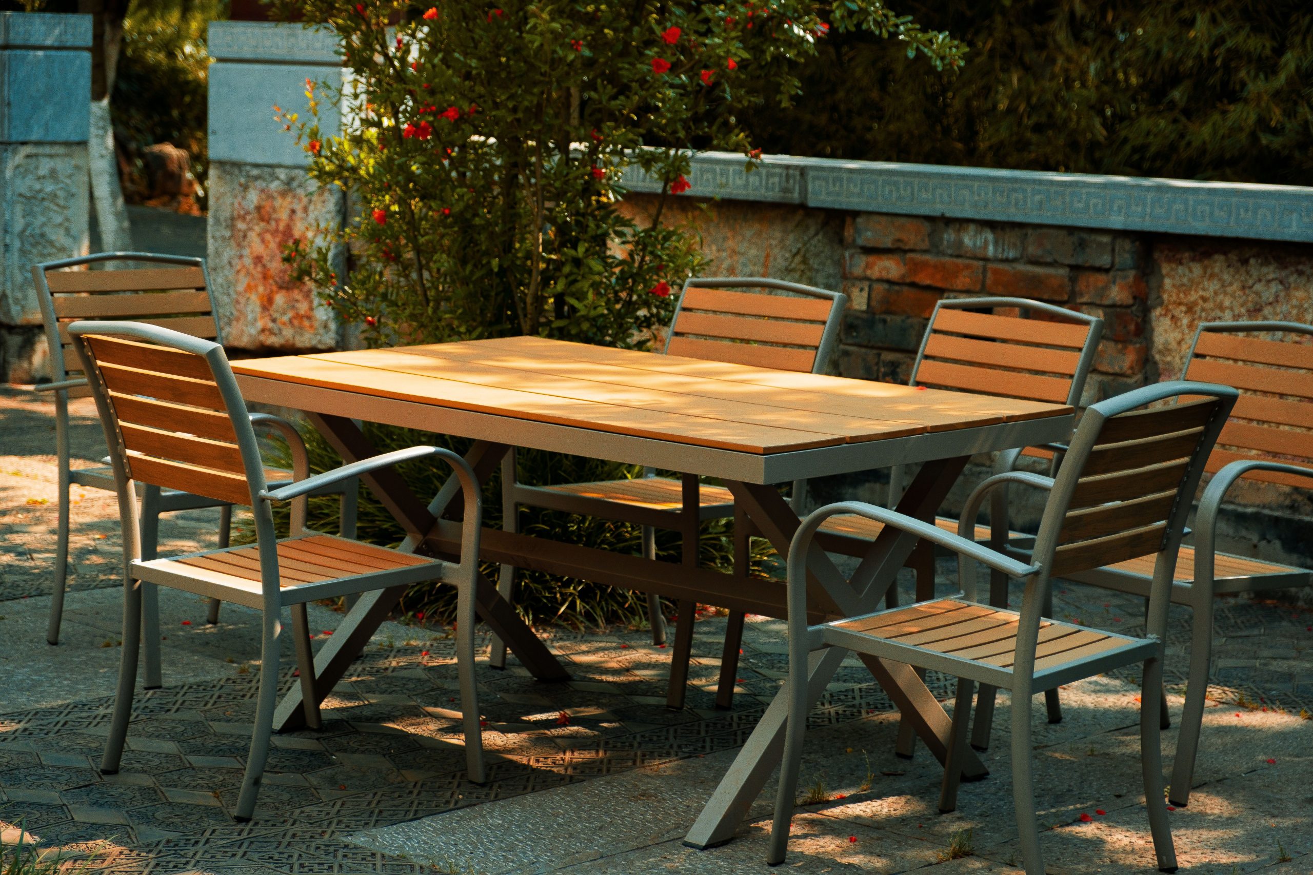 A serene outdoor patio setup featuring a wooden table and chairs amidst a garden setting.