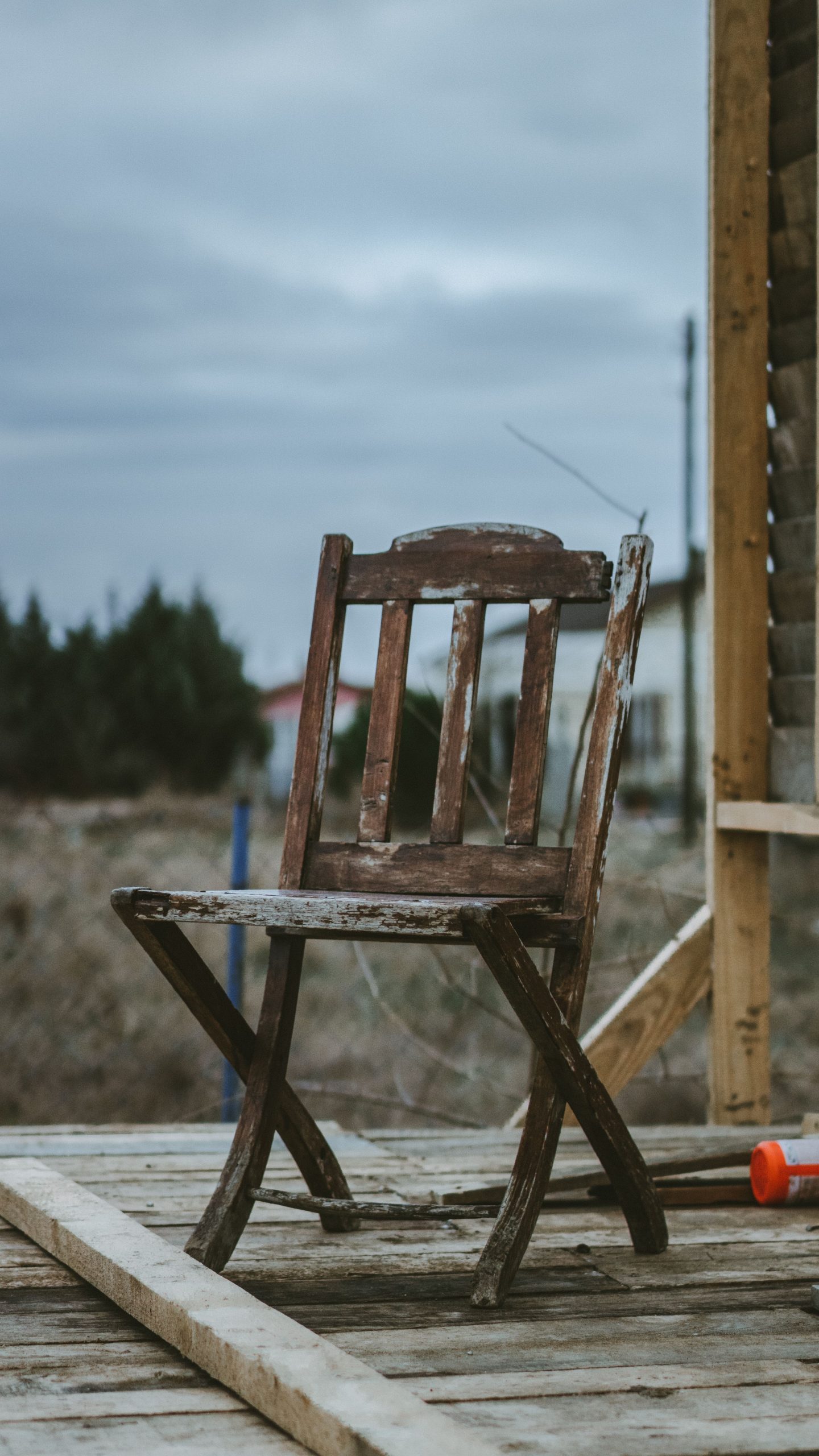 A solitary, aged wooden chair sits outside on a rustic porch under an overcast sky.