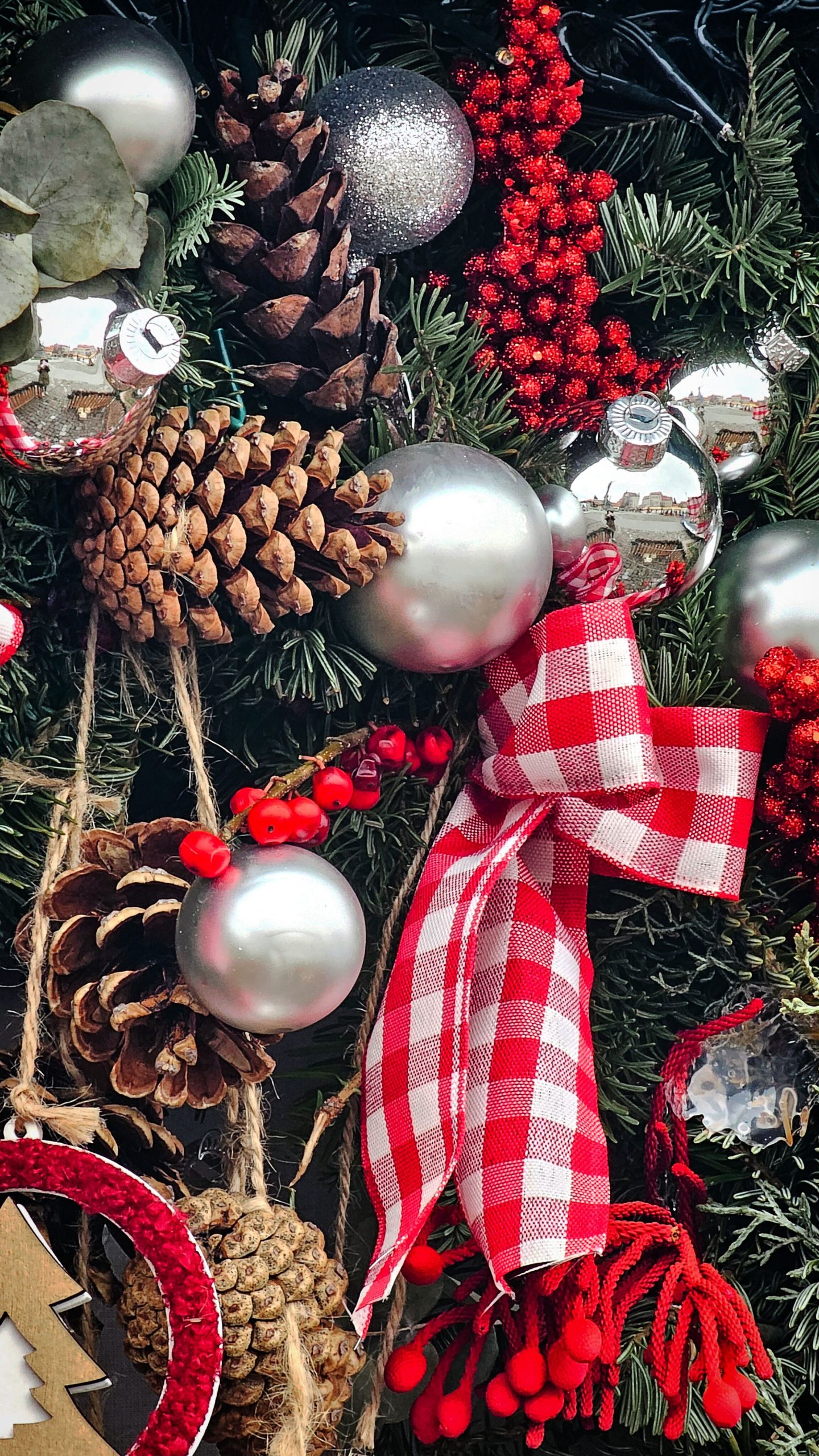 A vibrant Christmas wreath featuring pinecones, red ribbon, and silver ornaments.