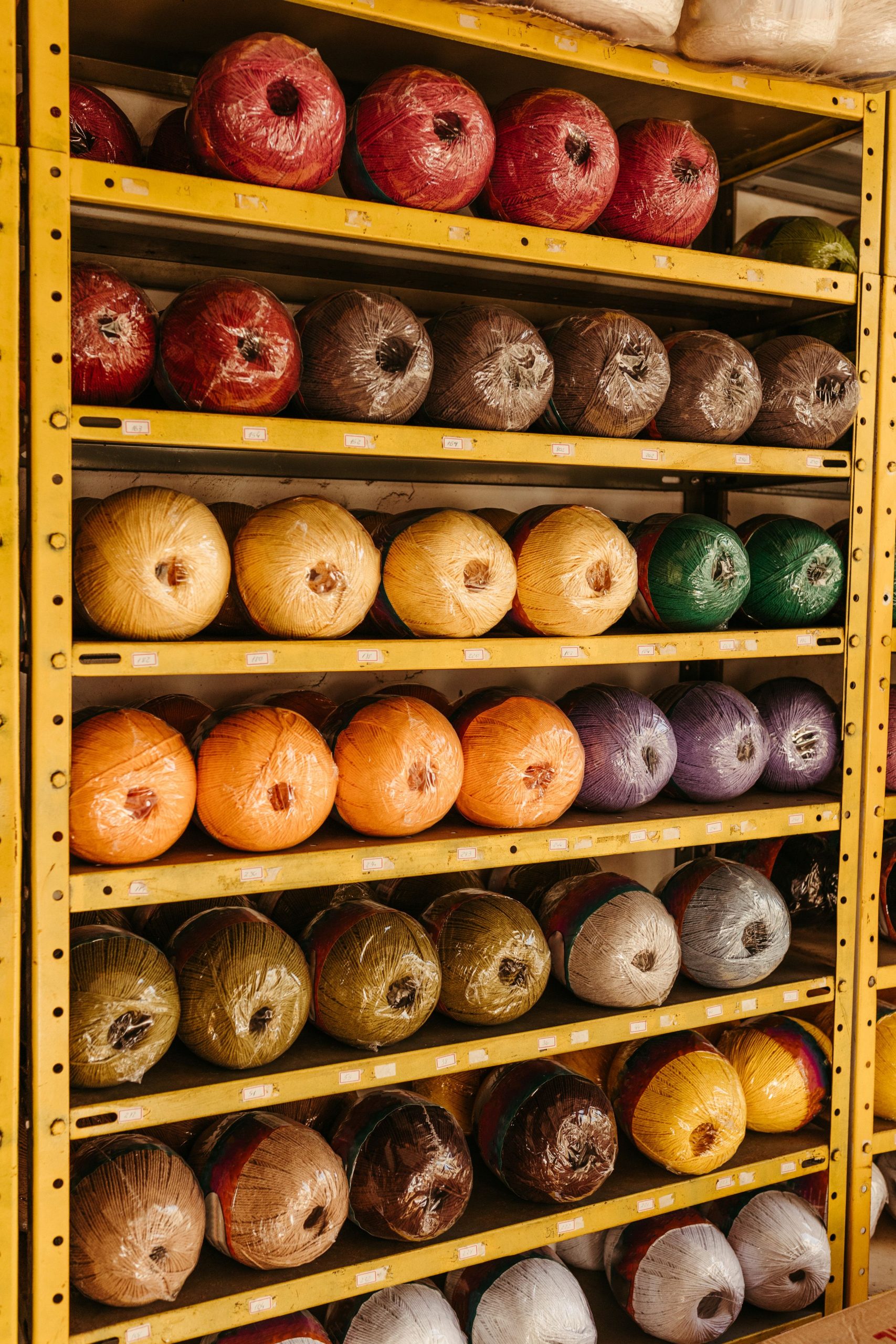 A vibrant display of multi-colored yarn rolls neatly arranged on industrial shelves in a workshop setting.