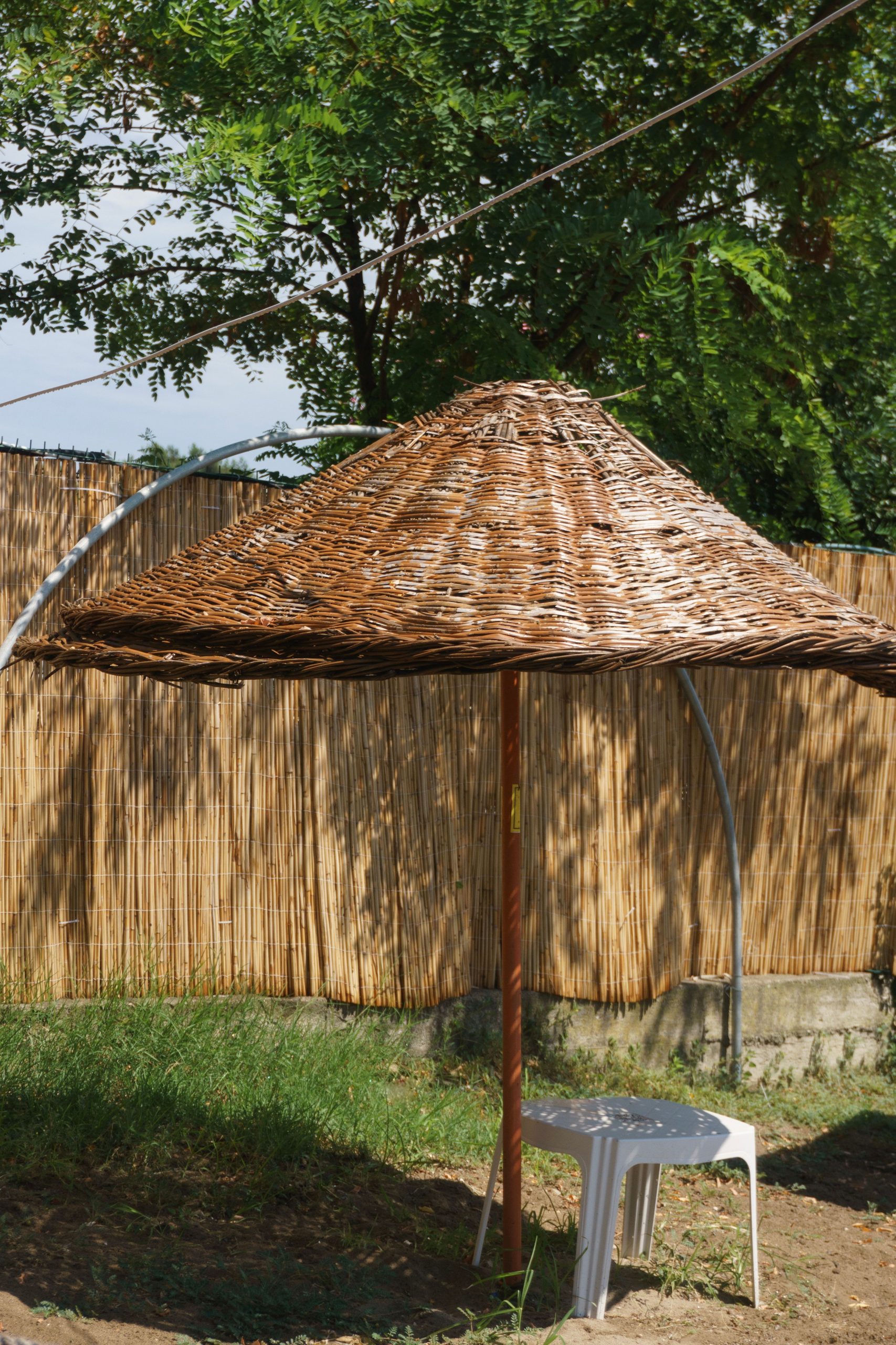 A wicker sunshade in a sunny garden with a bamboo fence and trees.