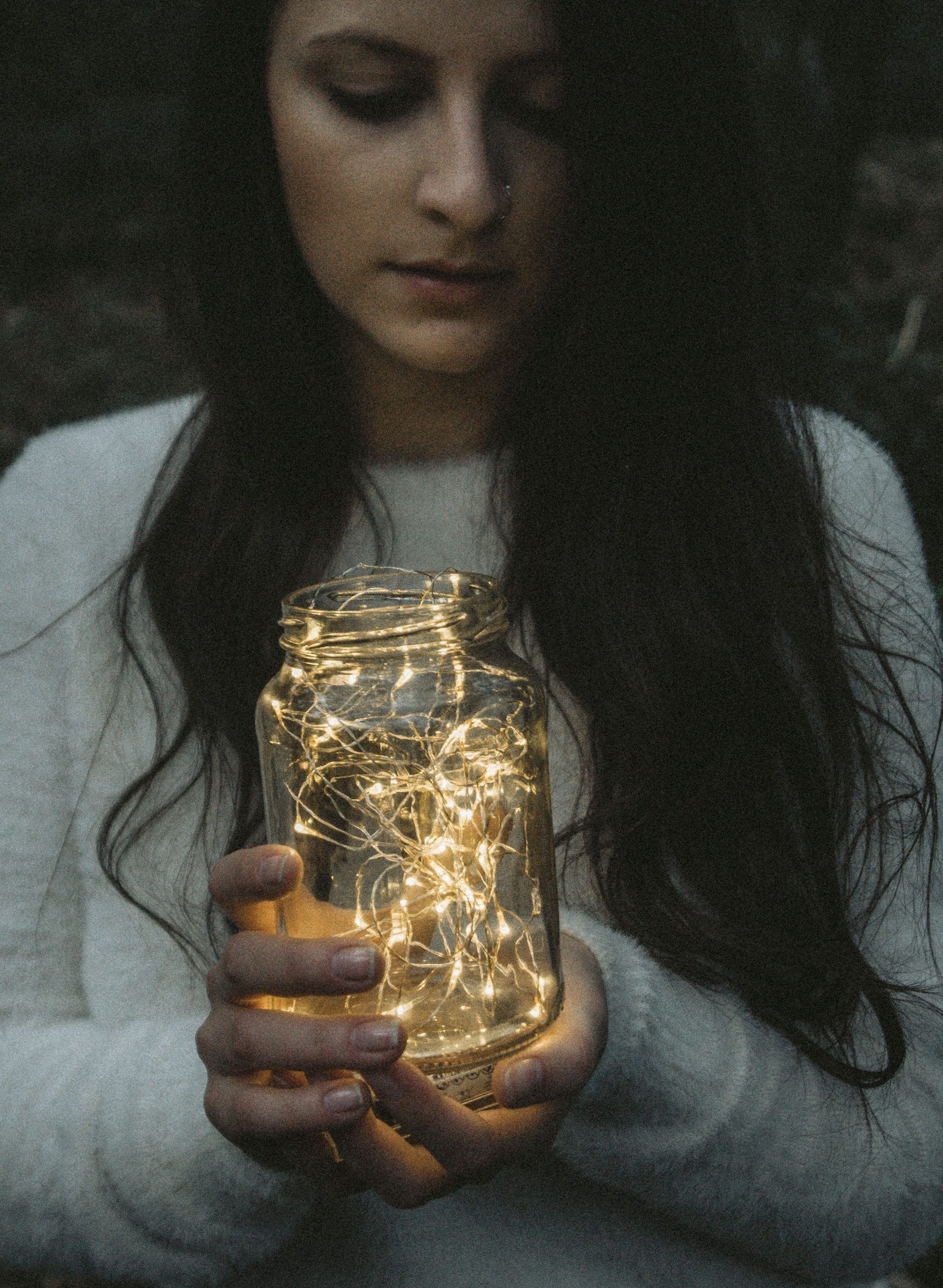 A woman holds a glowing jar outdoors in twilight, creating a warm and cozy ambiance.
