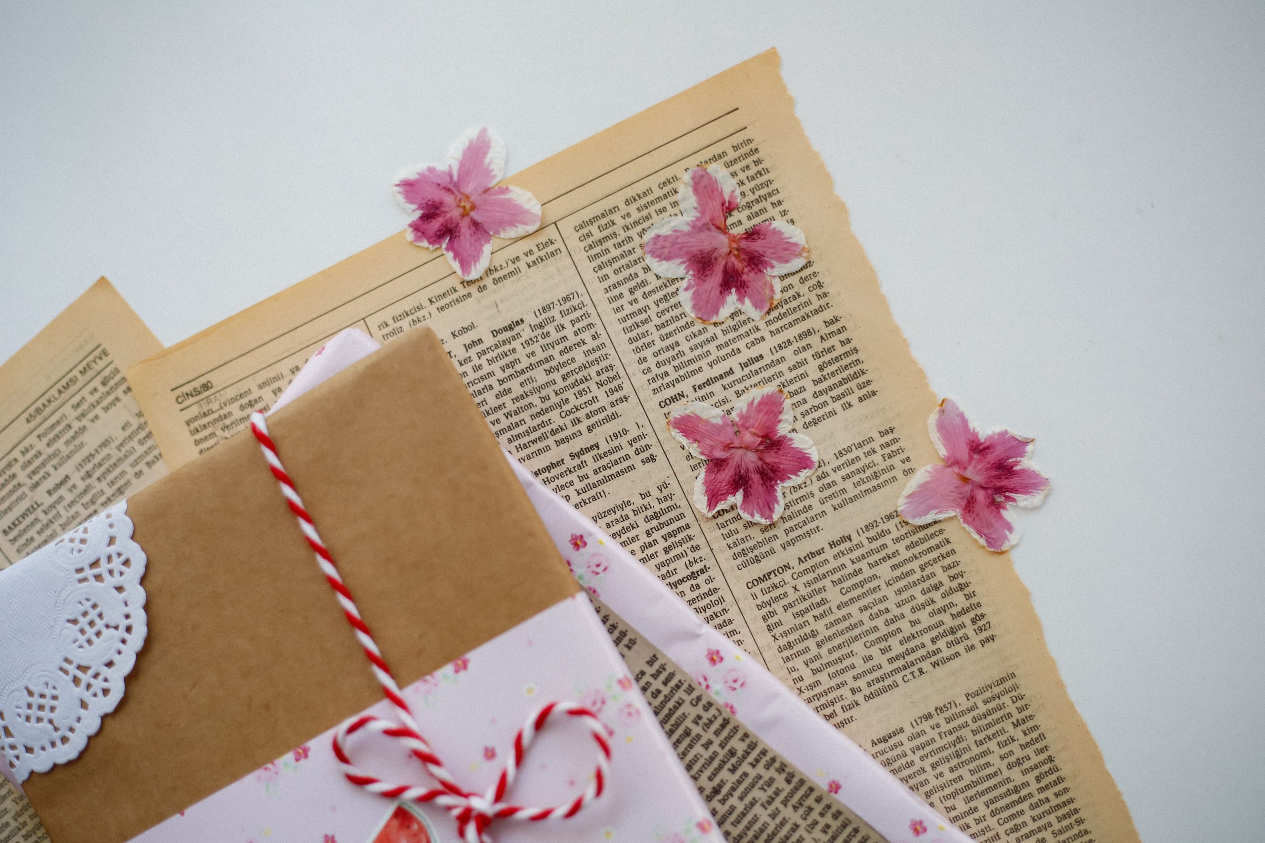 An artistic flat lay of a vintage-styled gift wrapped with pink flowers and old book pages.