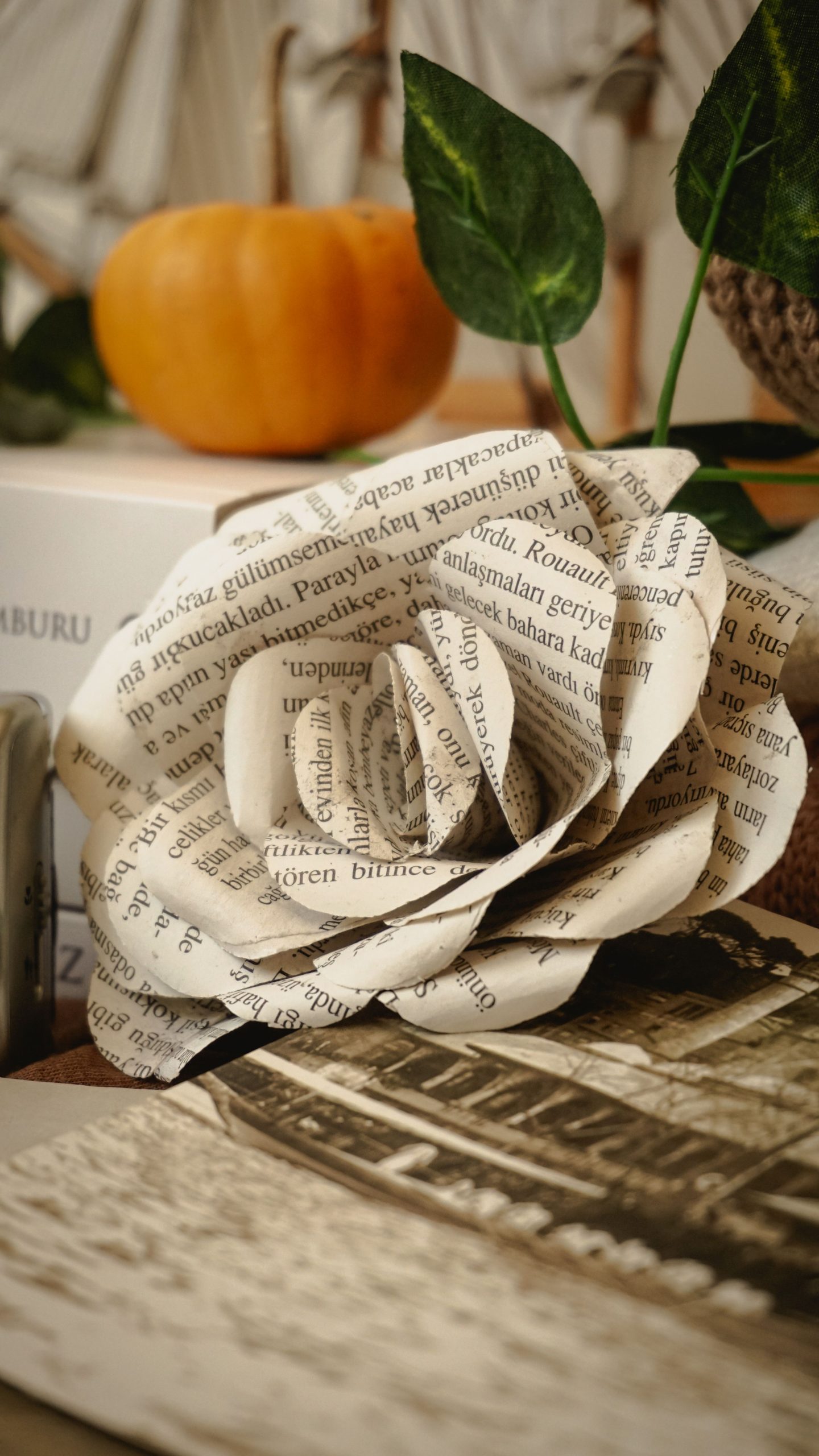 An artistic paper rose crafted from text pages with a warm, autumnal background.