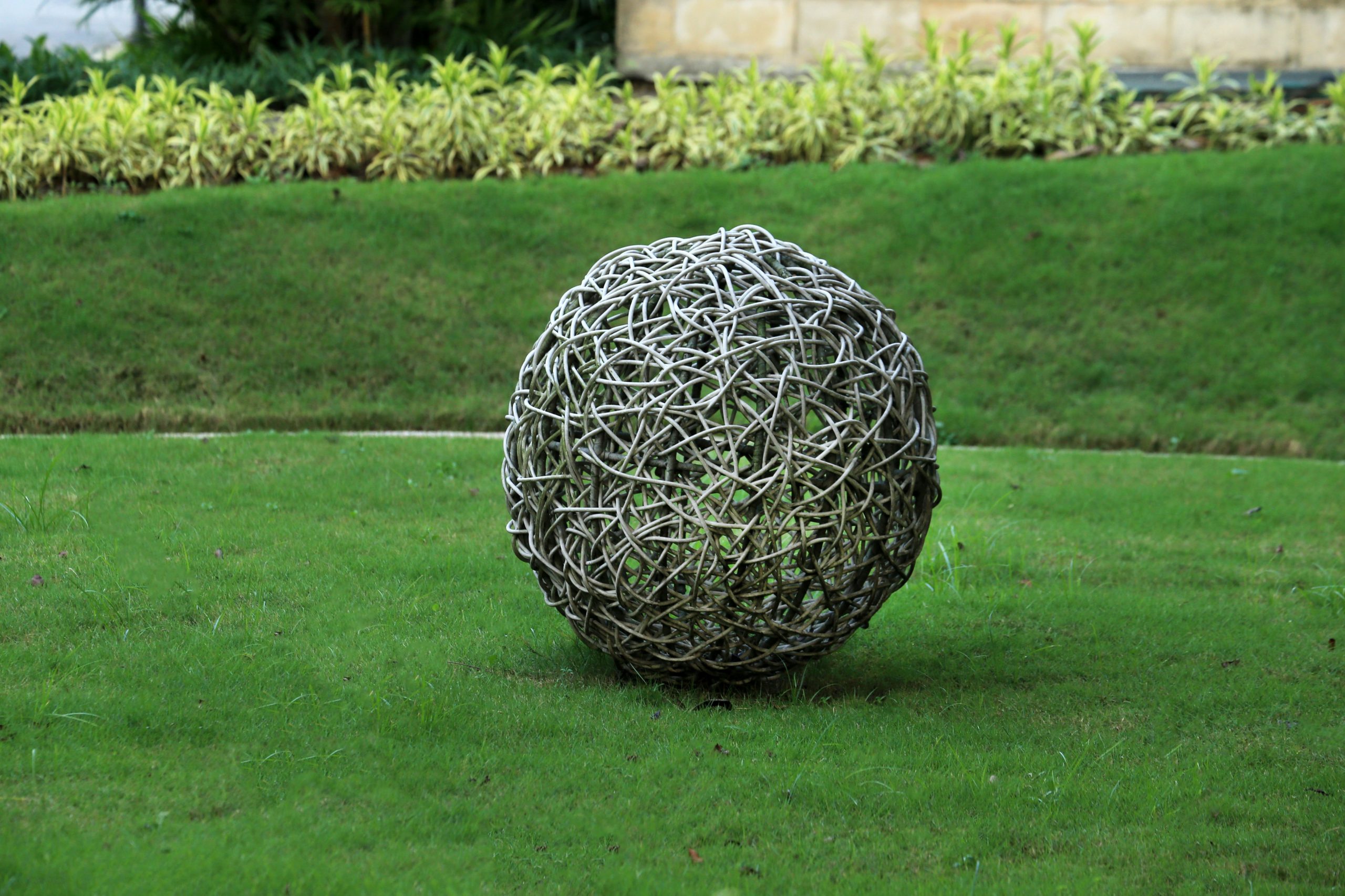 Artistic wicker ball sculpture elegantly placed in a lush garden setting.