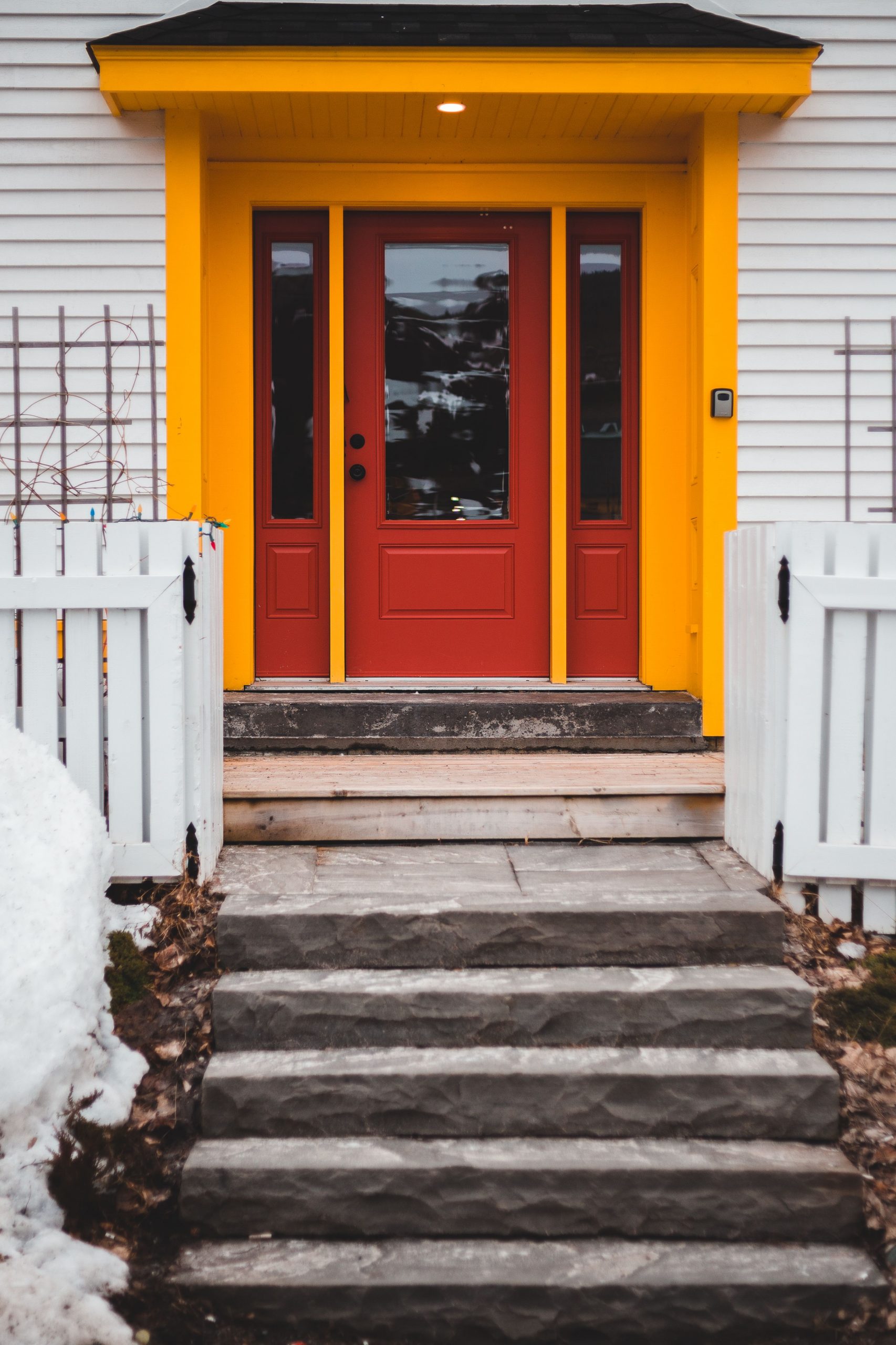 Bright red door with yellow framing on a winter day, highlighting a cozy home entrance.