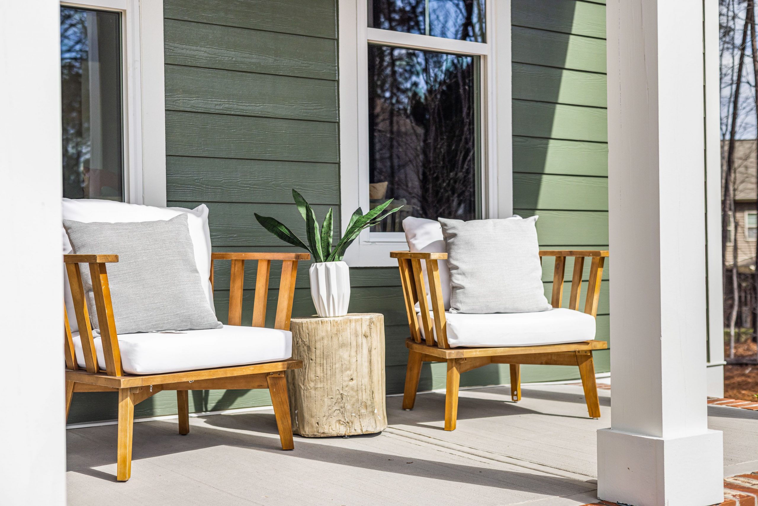 Charming porch featuring wooden armchairs, a rustic table, and a potted plant against green siding.