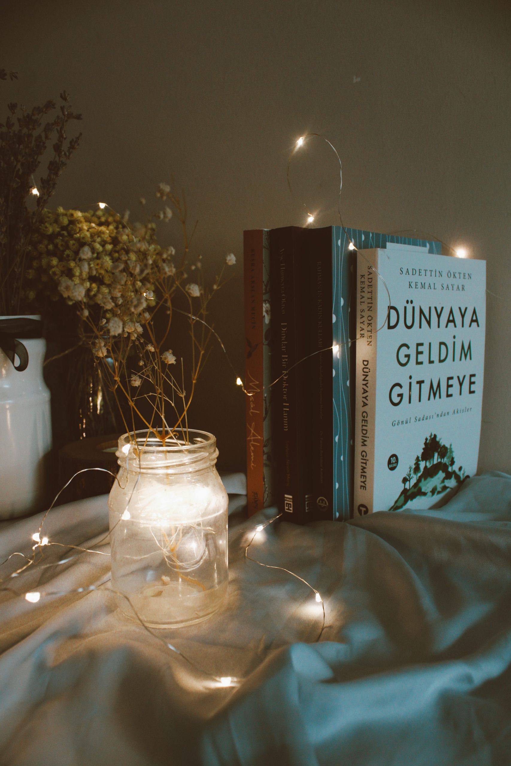 Charming setup of books, jar with lights, and dried flowers creating a cozy indoor ambiance.