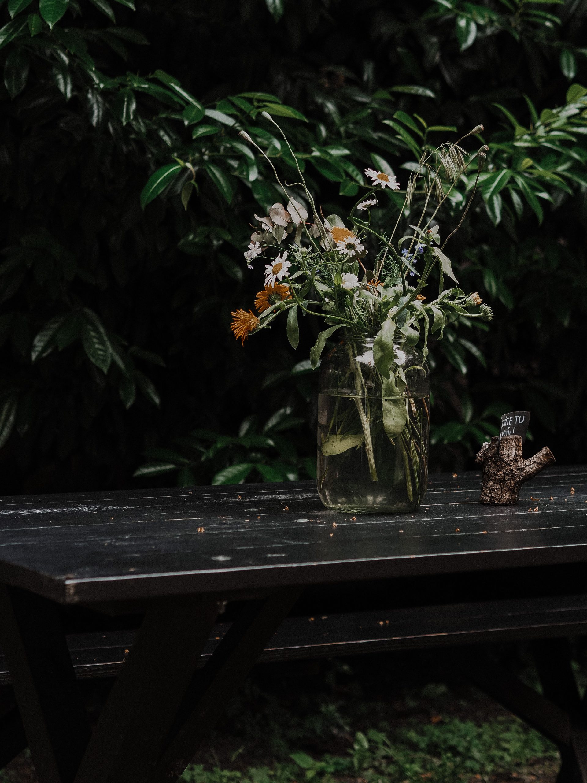 Charming wildflower bouquet in a glass jar on a rustic outdoor table with lush green background.