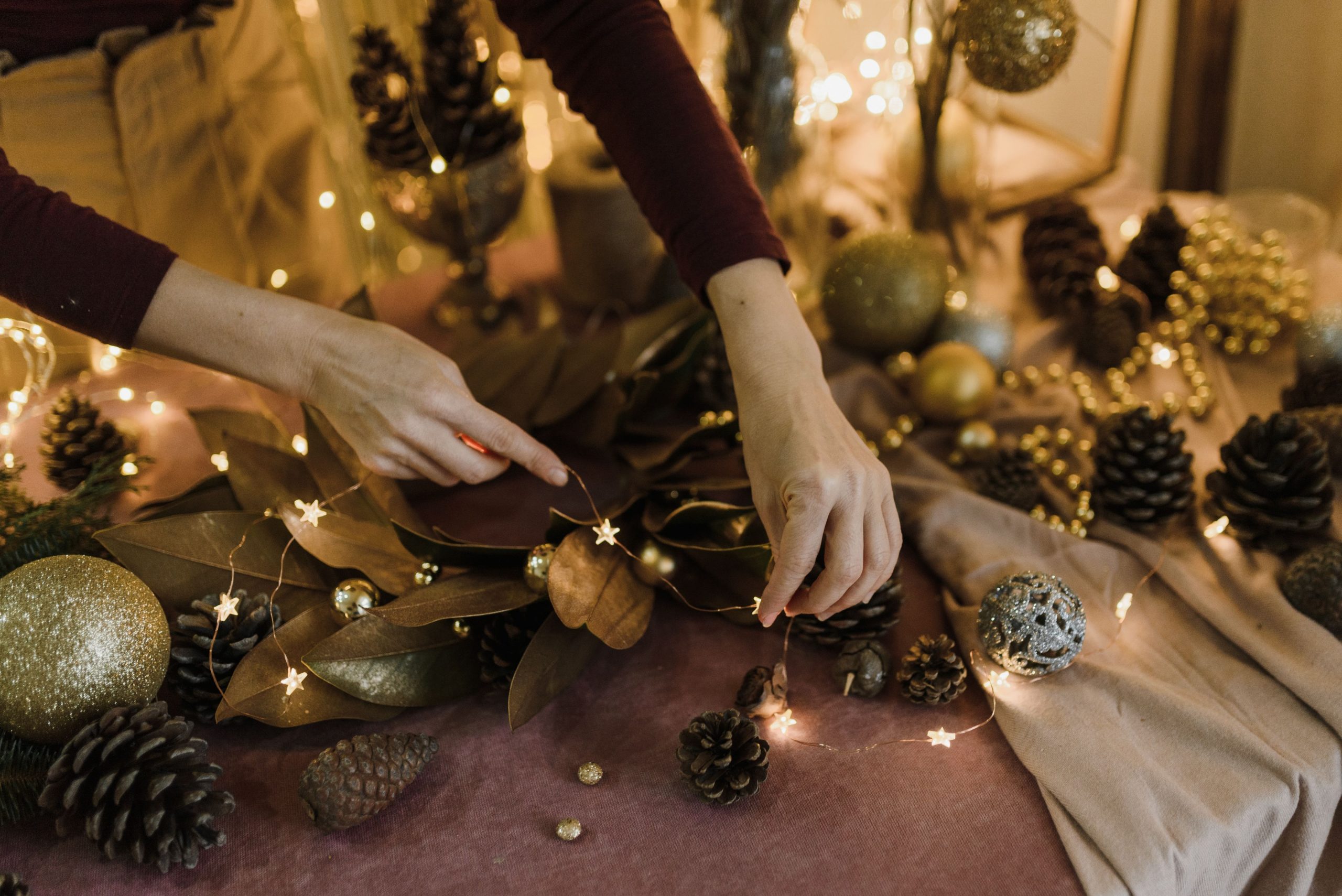 Close-up of hands arranging decorative lights and pinecones for a festive table setting.