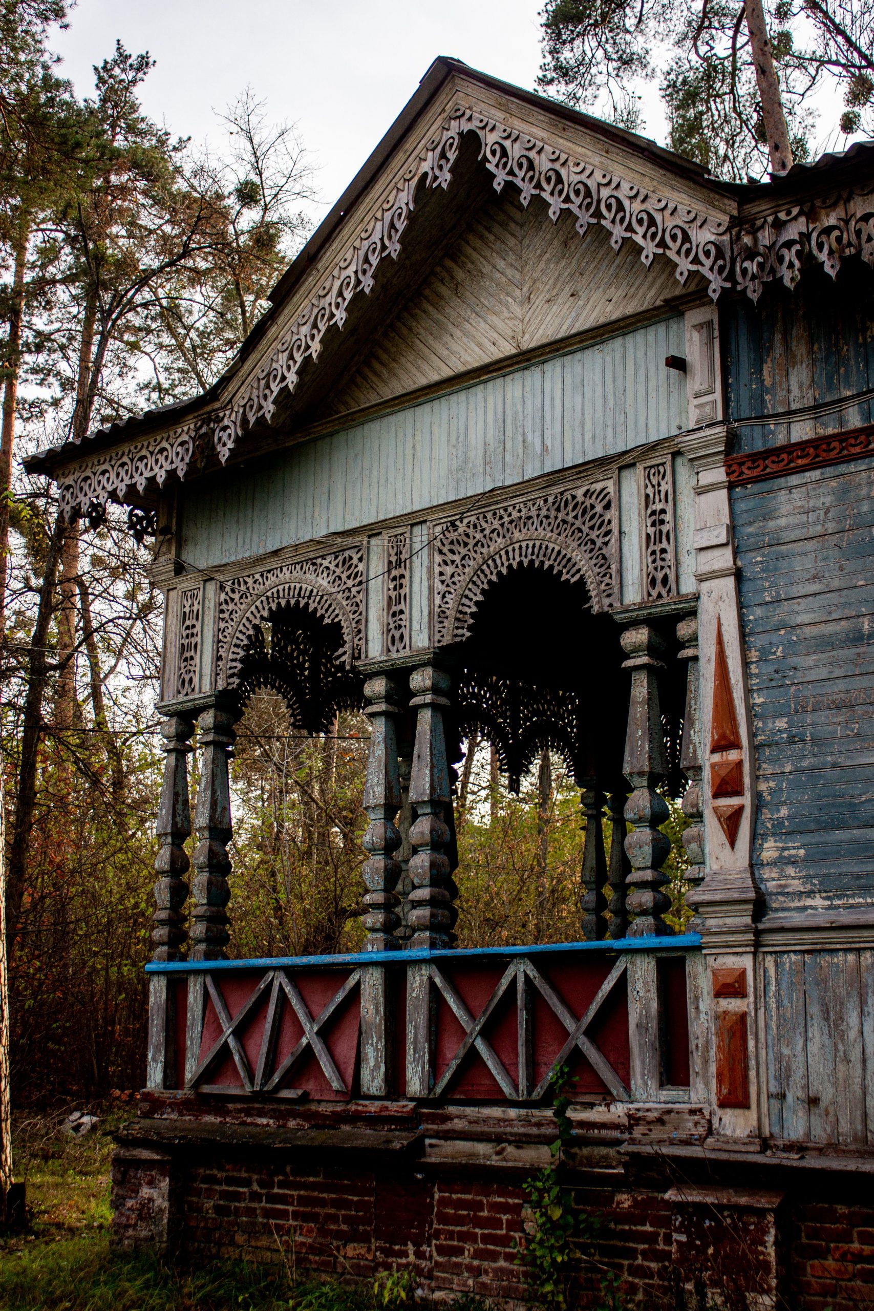 Decorative wooden porch with intricate detailing set in a rustic, forested area.