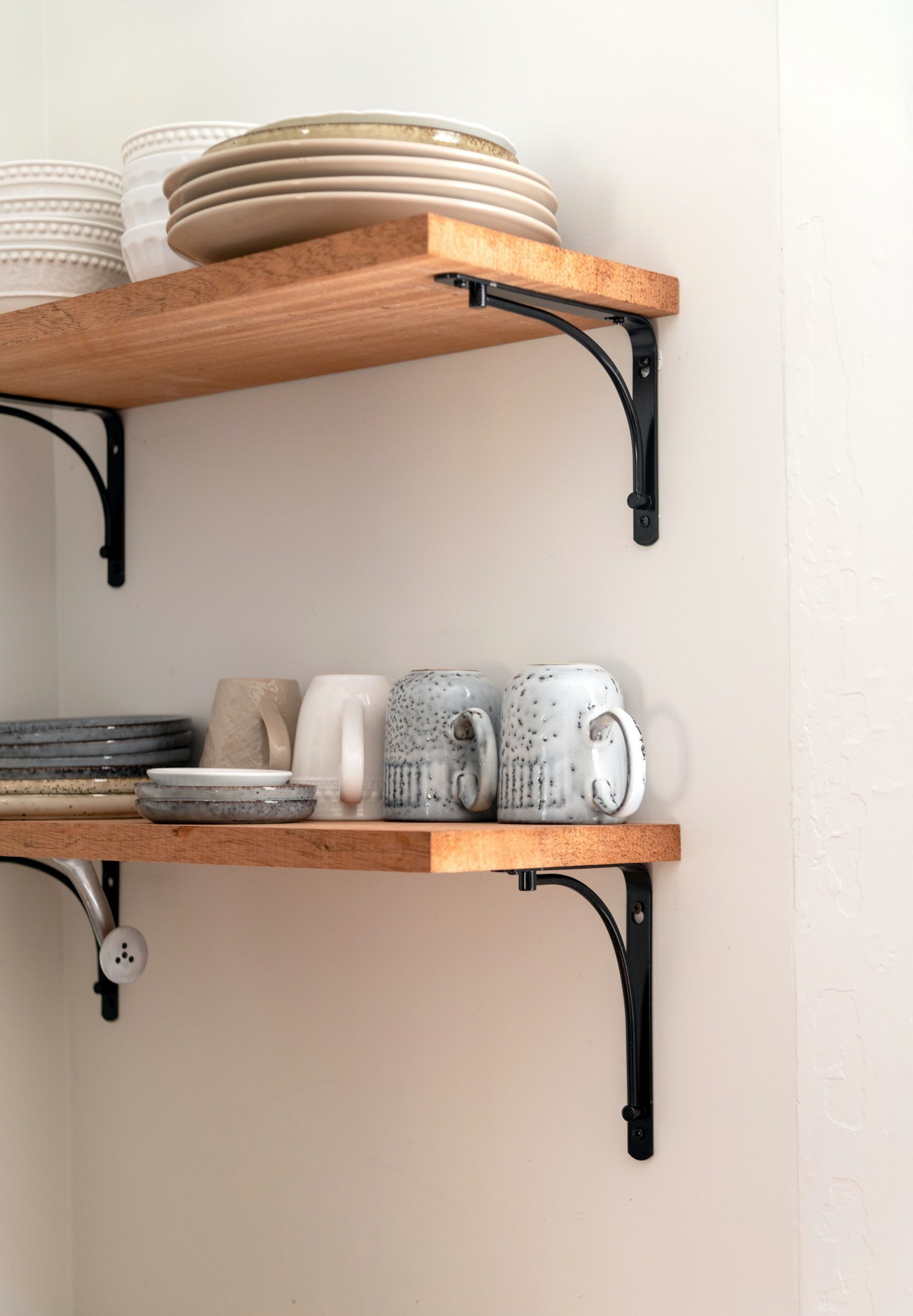 Elegant arrangement of ceramic crockery on wooden shelves in a rustic kitchen setting.