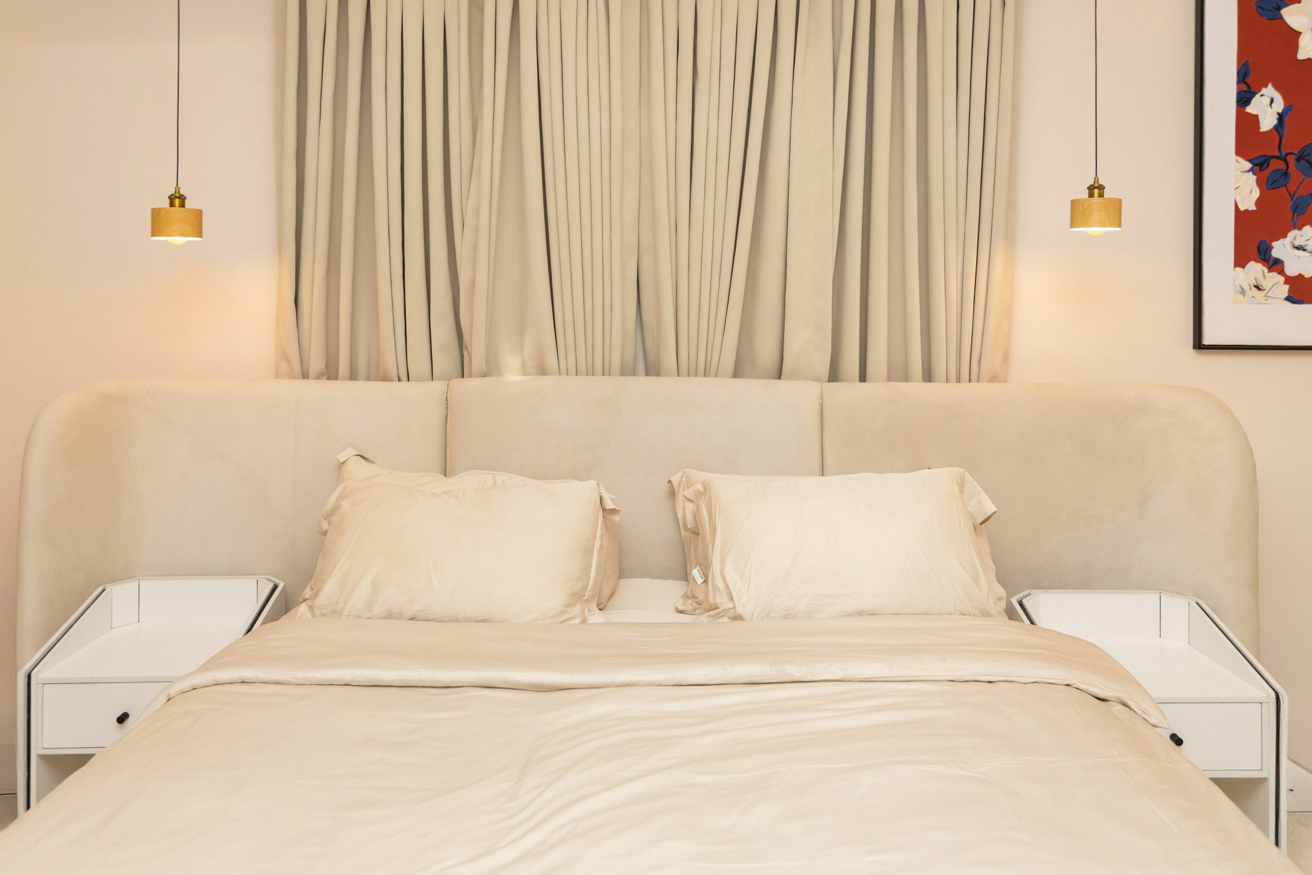 Elegant beige bed with white nightstands and pendant lights.