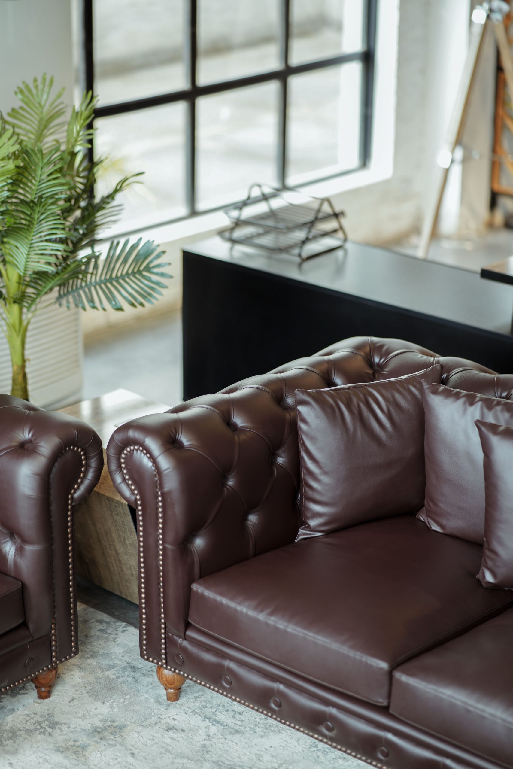 Elegant modern living room featuring a luxurious brown leather sofa beside a window with natural light.