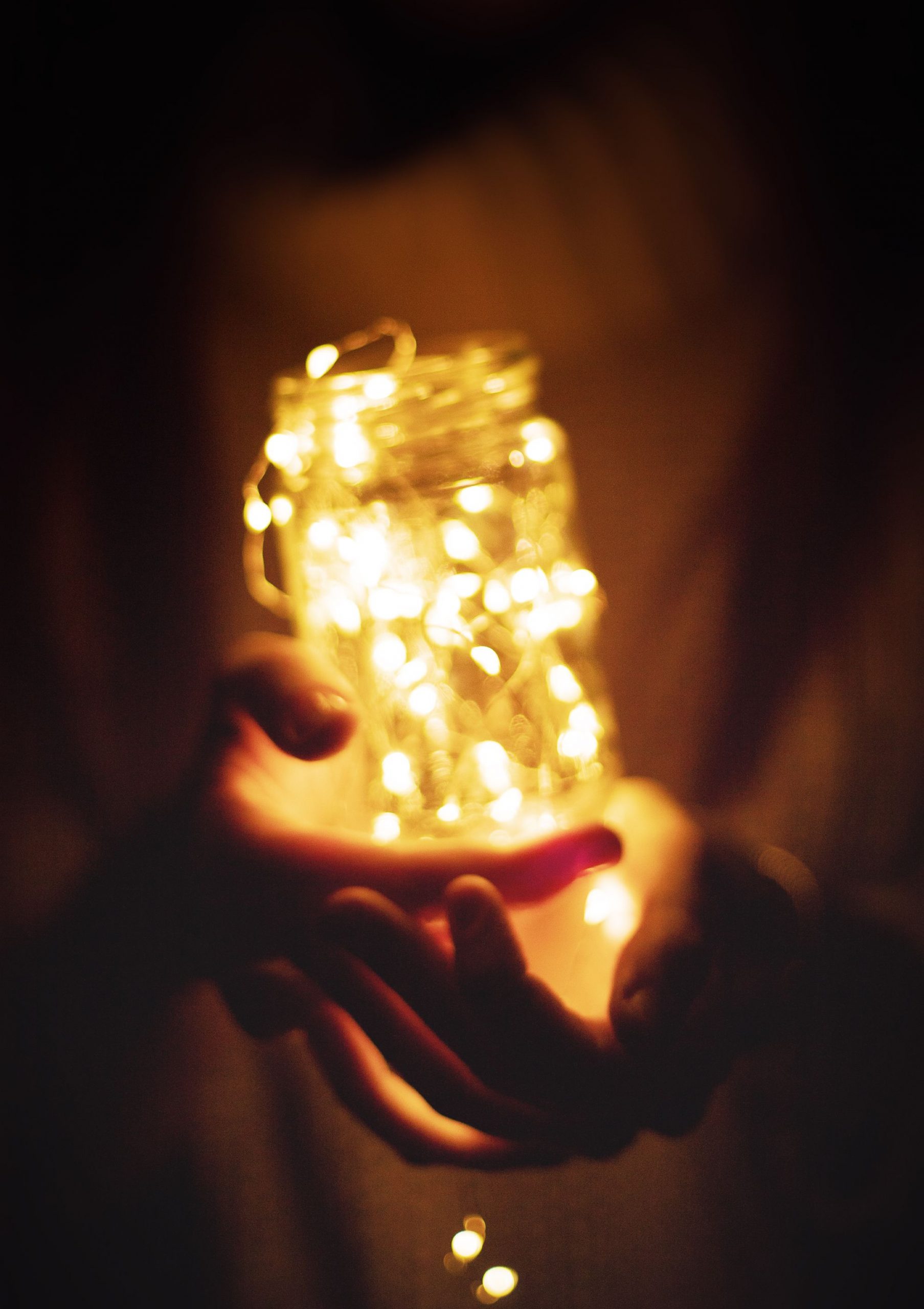 Enchanting hands holding an illuminated glass jar filled with warm string lights, creating a magical glow.