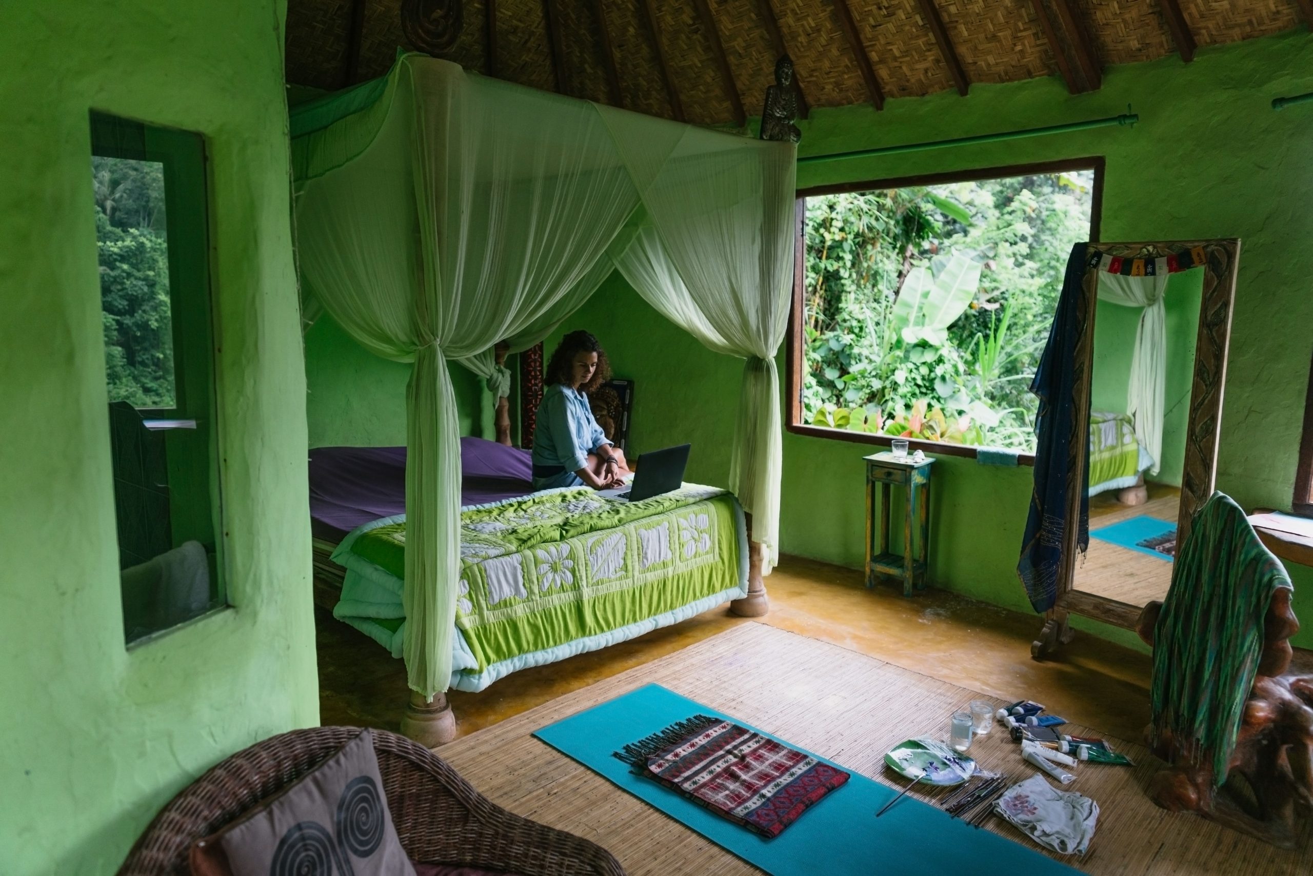 Full body female resting on comfy bed with netbook while spending day in cozy green room of rural cottage located amidst exotic rainforest