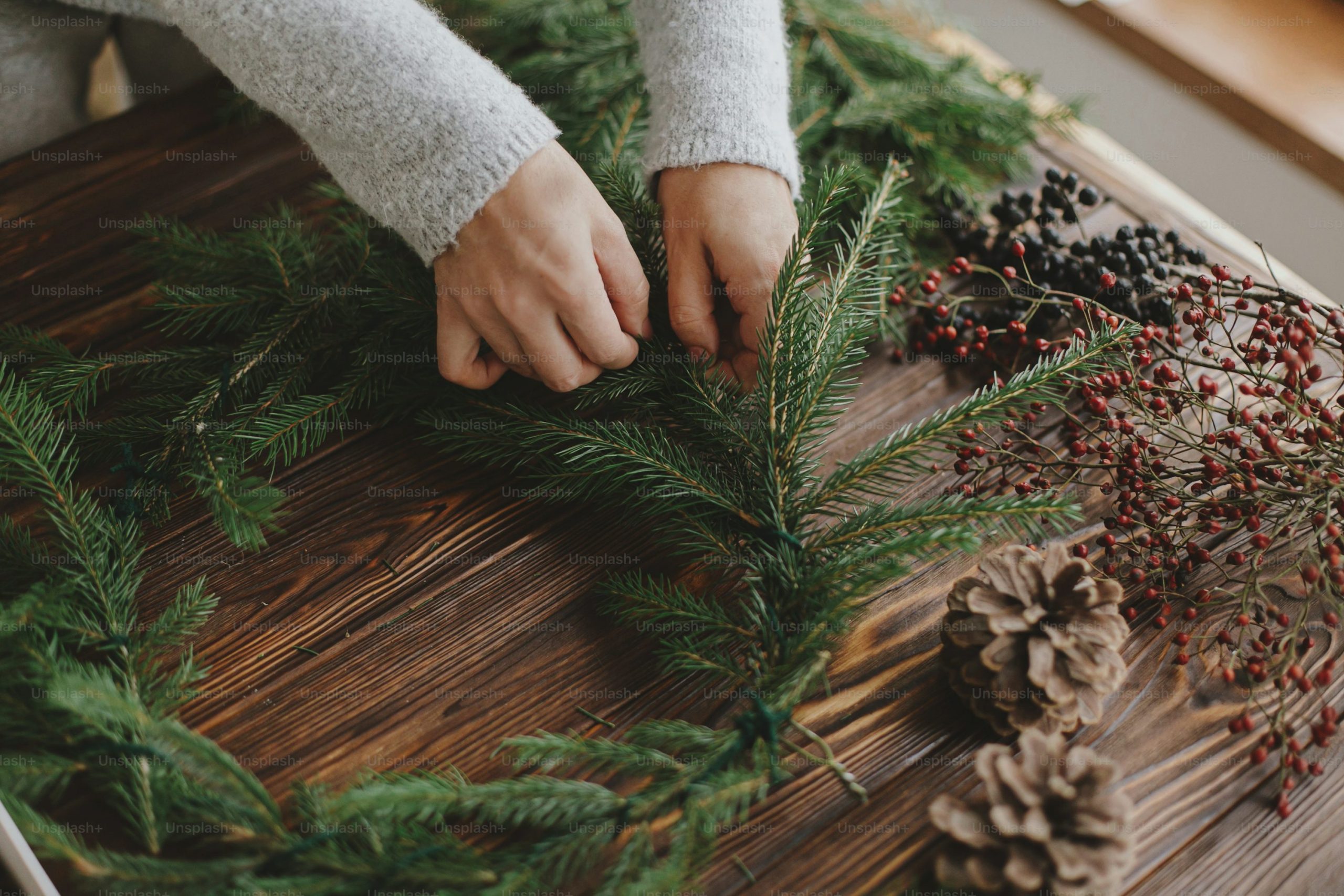 Hands holding green fir branches on rustic wooden table with pine cones, berries, natural festive decorations. Making rustic christmas wreath. Seasonal winter workshop, holiday advent photo – Christ