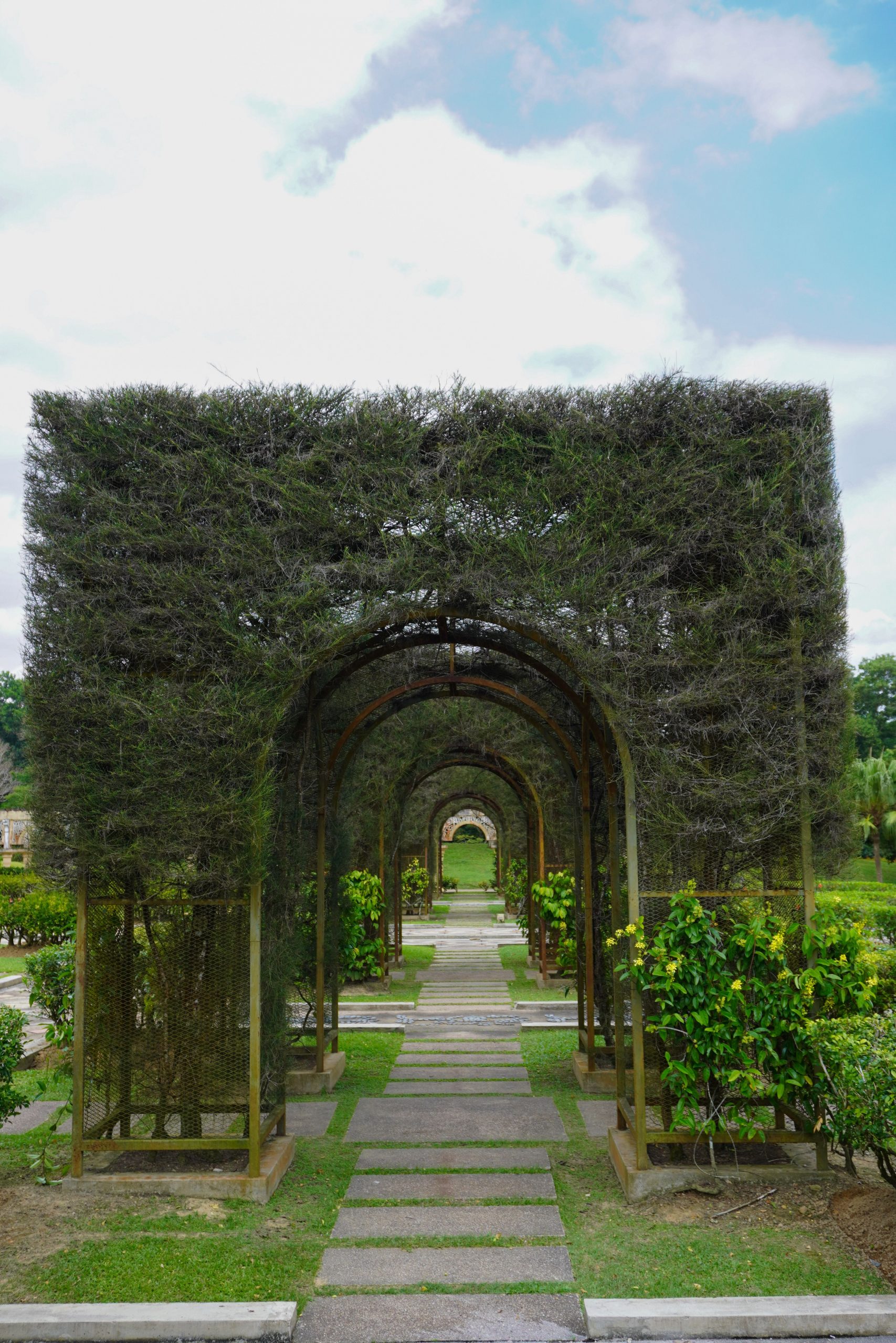 Lush green pergola arches over a serene path in Taman Botani, Johor, Malaysia.