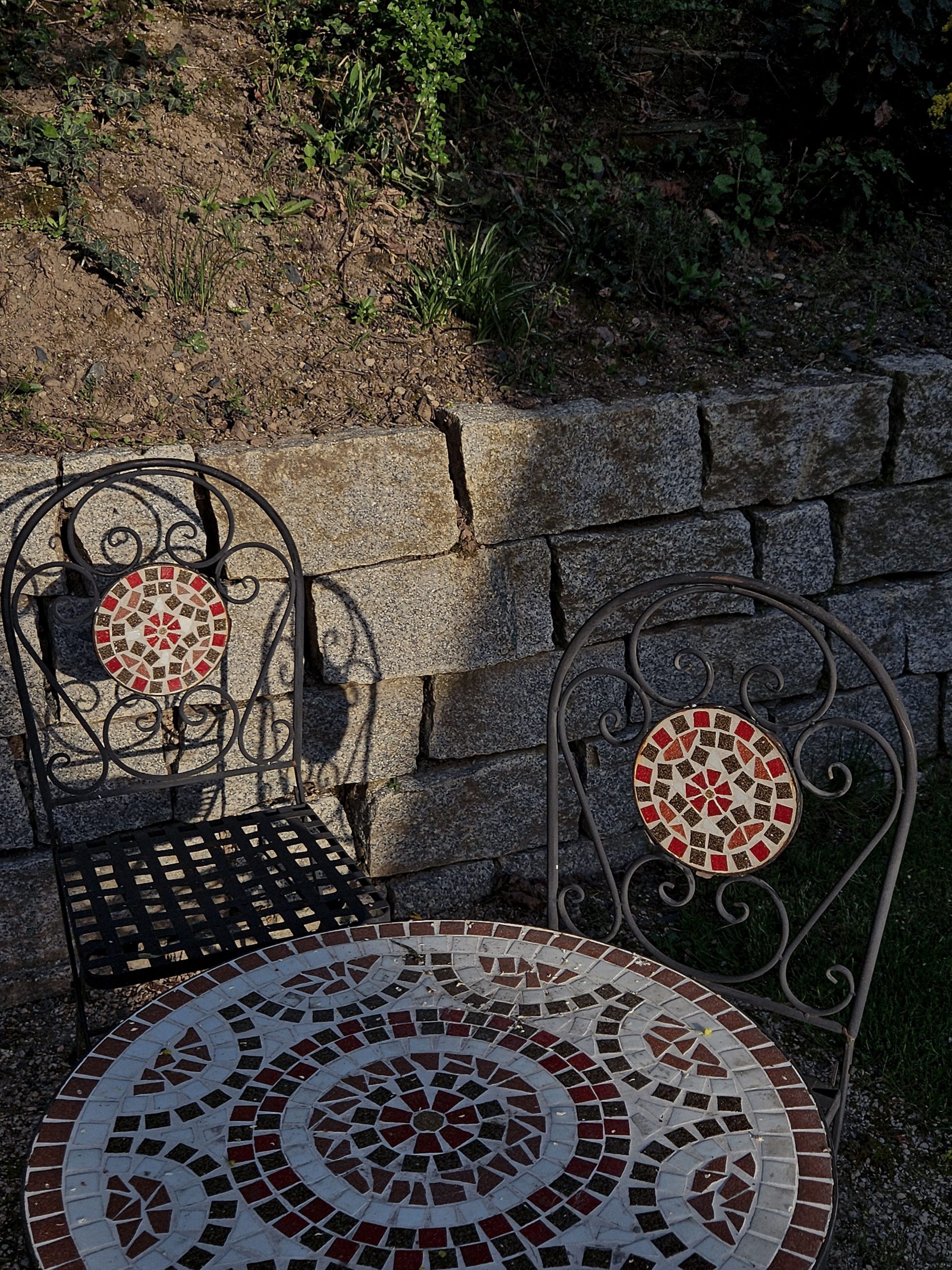 Ornate mosaic table and chairs in a sunny outdoor stone patio.