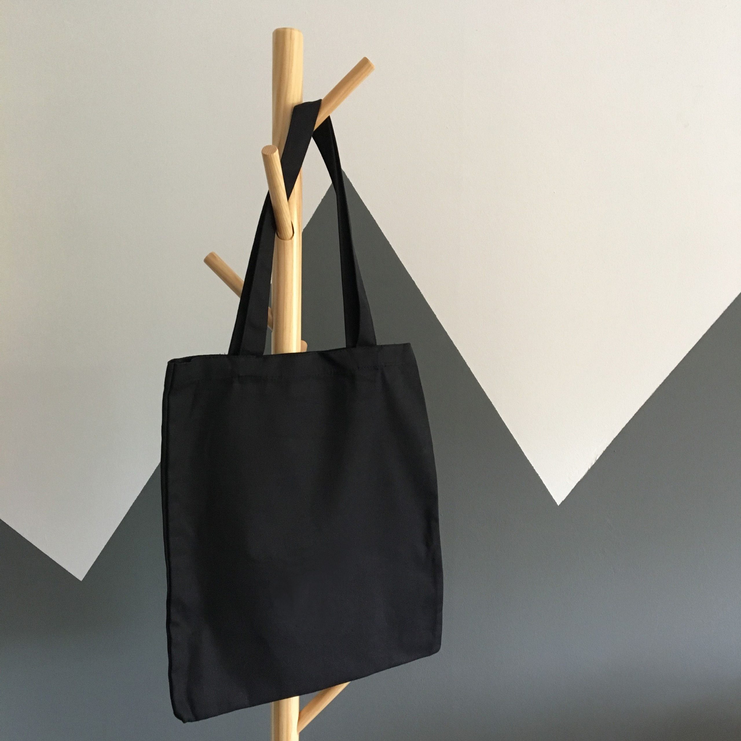 Simple and elegant black canvas tote bag hanging on a wooden rack, perfect for eco-friendly shopping.