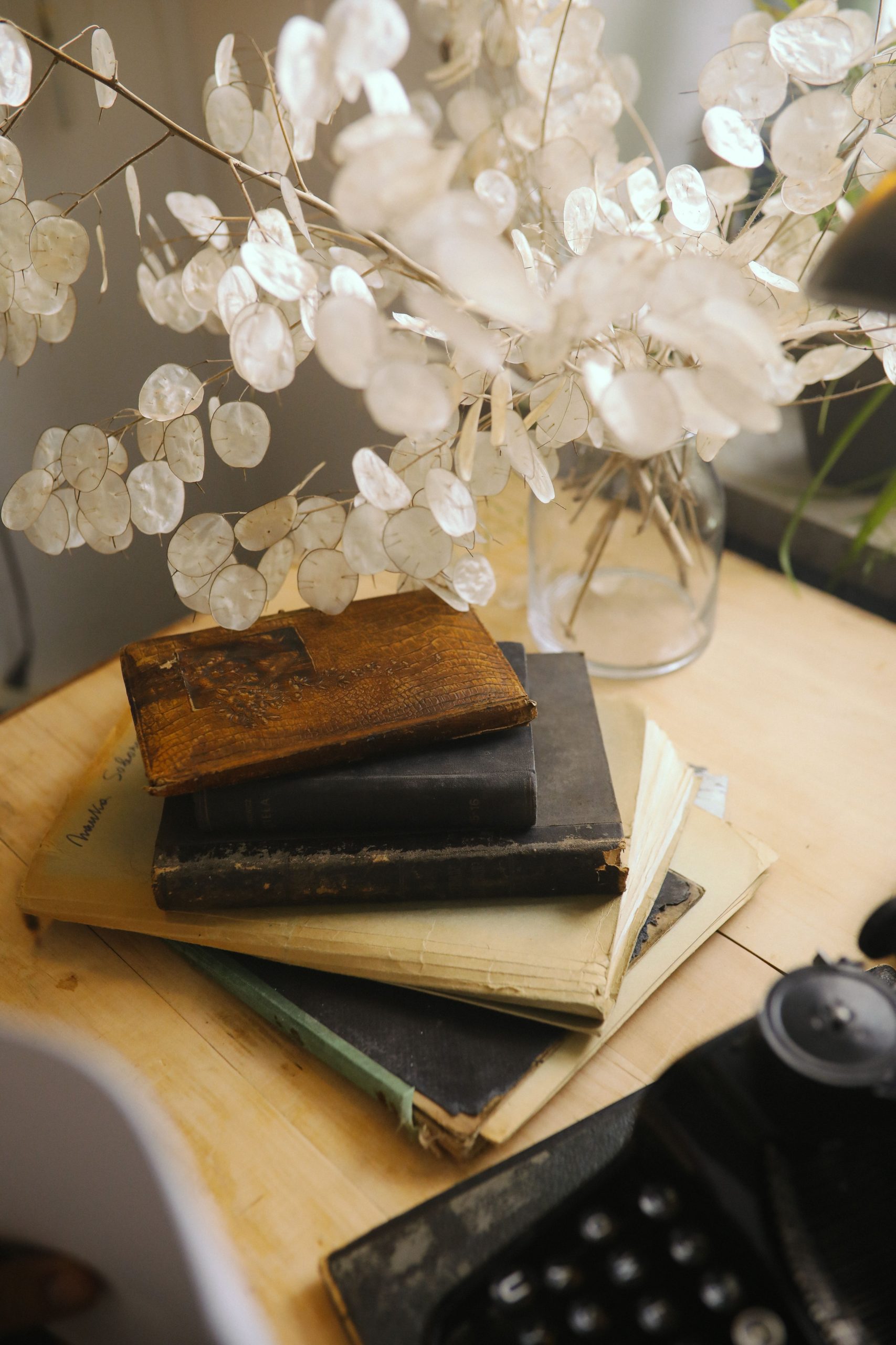 Stack of vintage books with delicate white flowers on a wooden desk. Calm and serene atmosphere.