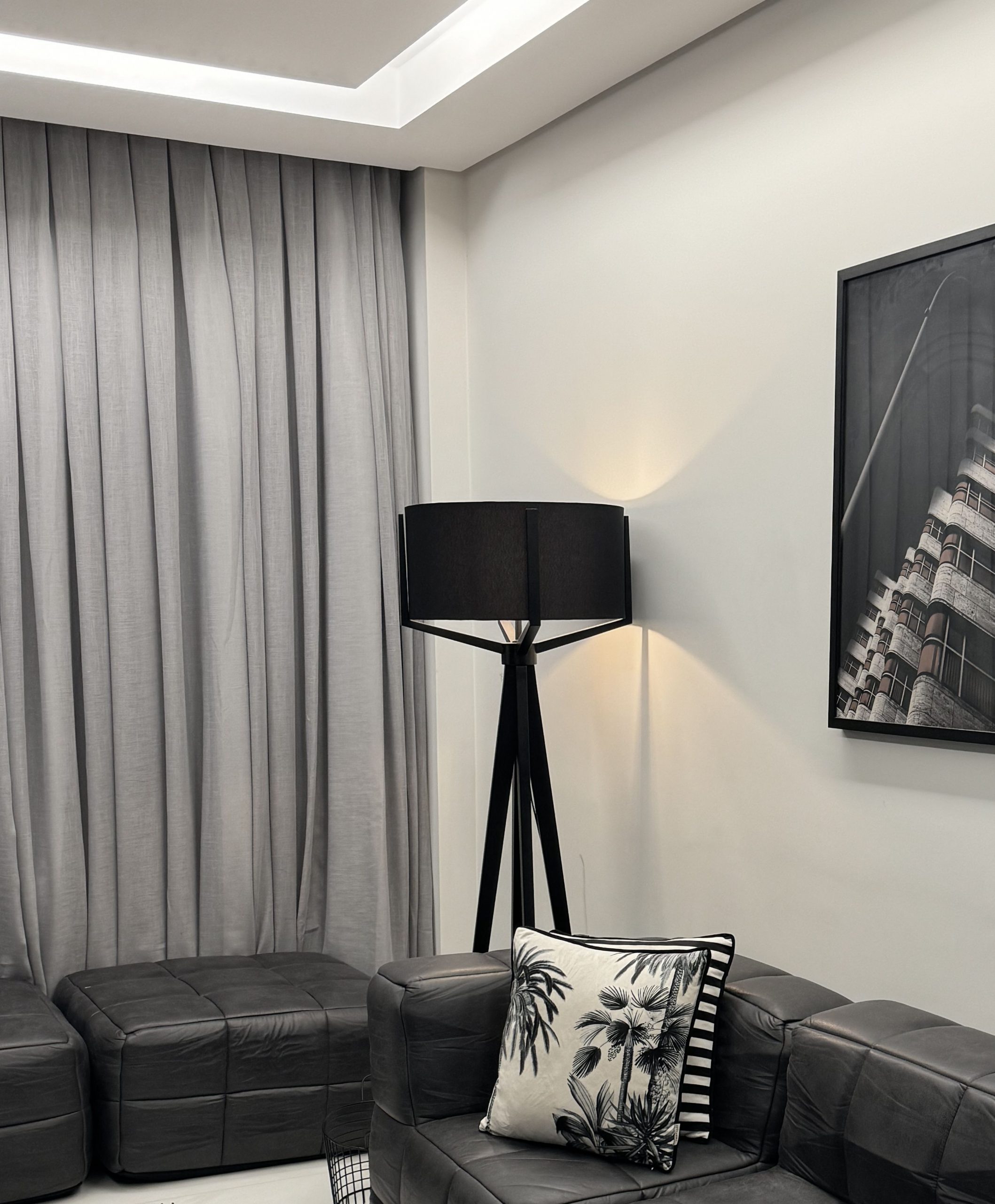 Stylish modern living room featuring black leather sofa and a floor lamp against gray curtains.