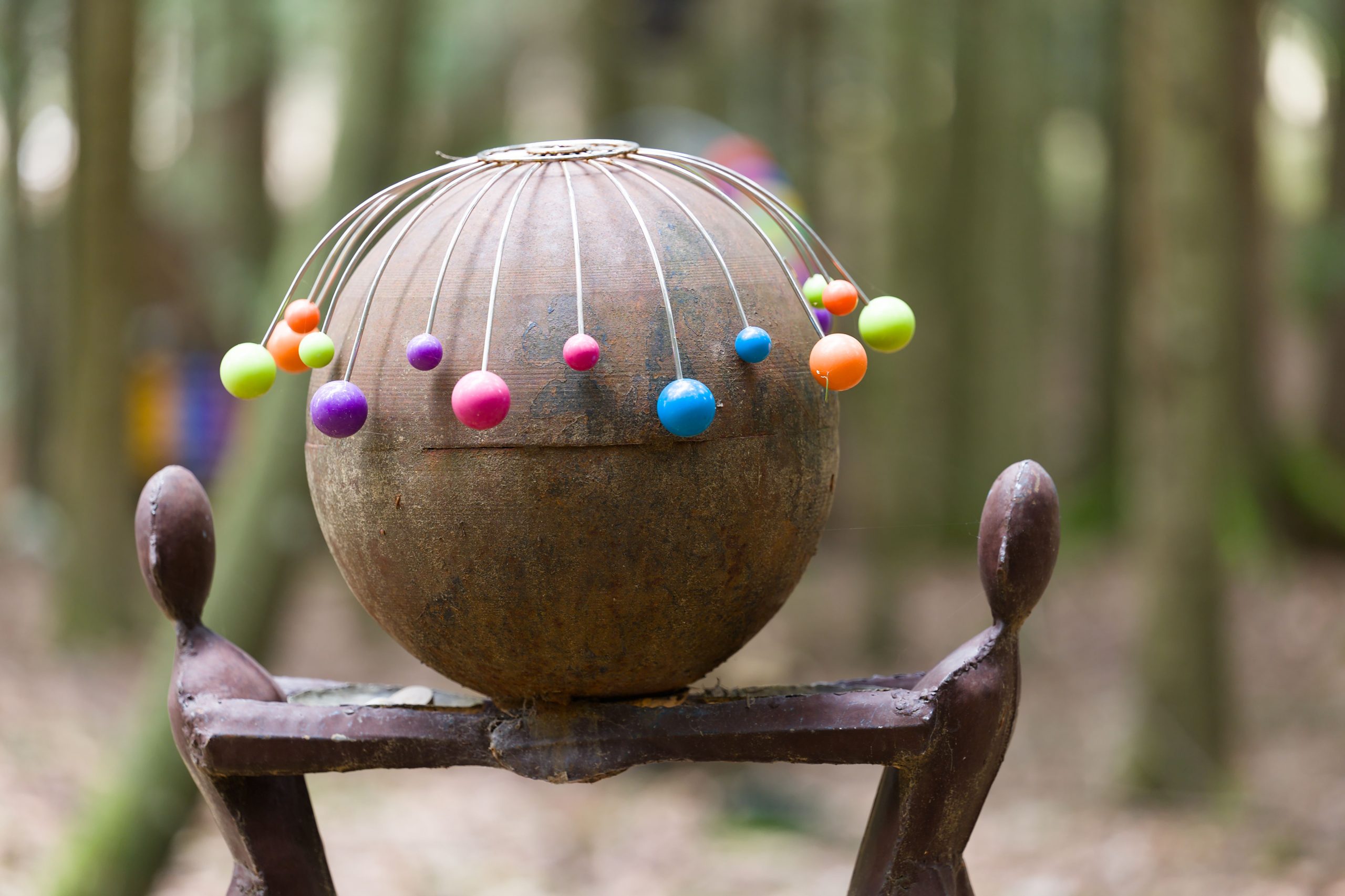 Unique sculpture with colorful elements in a serene forest setting.