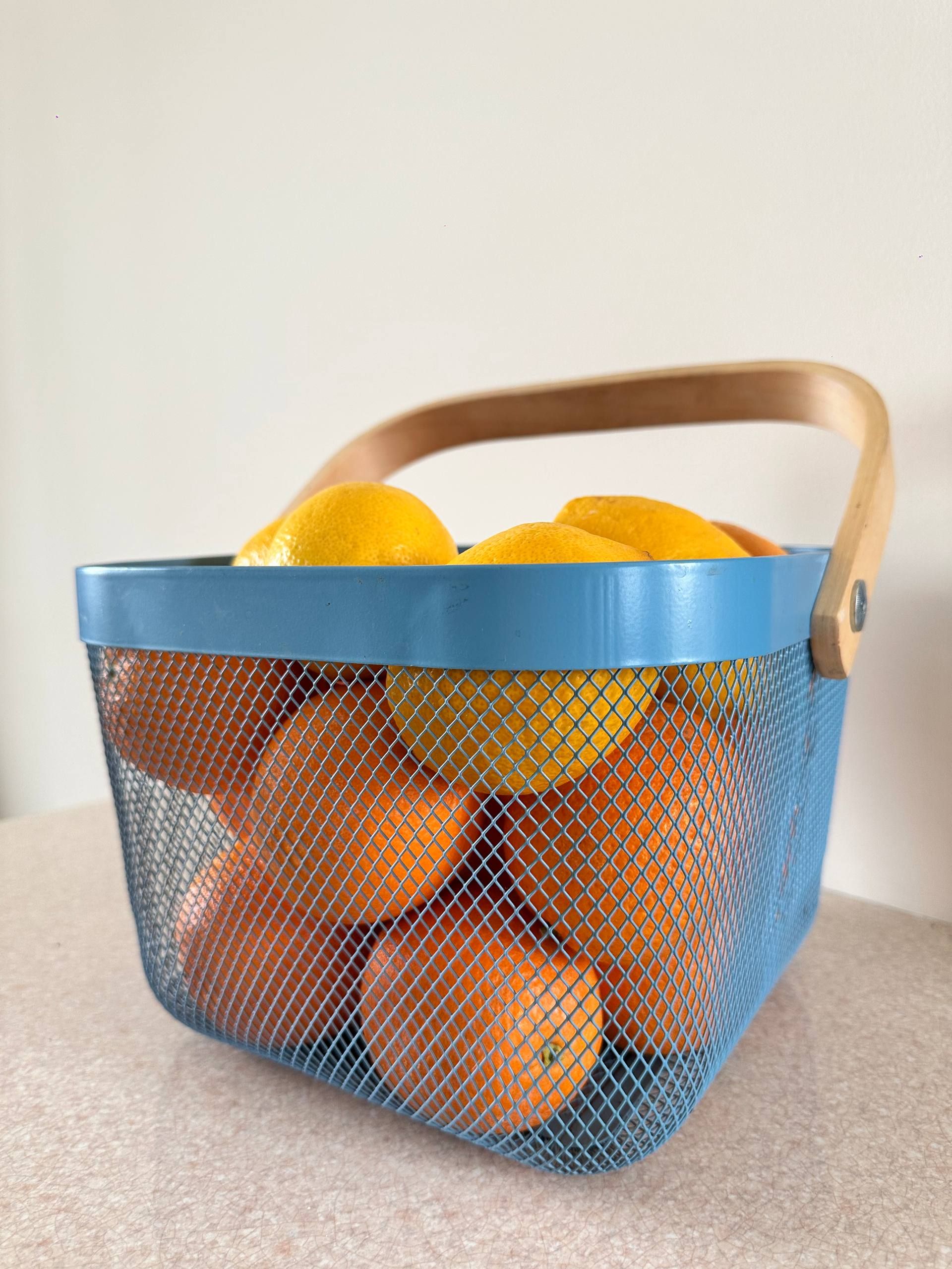 Vibrant lemons and oranges in a stylish blue metal basket.
