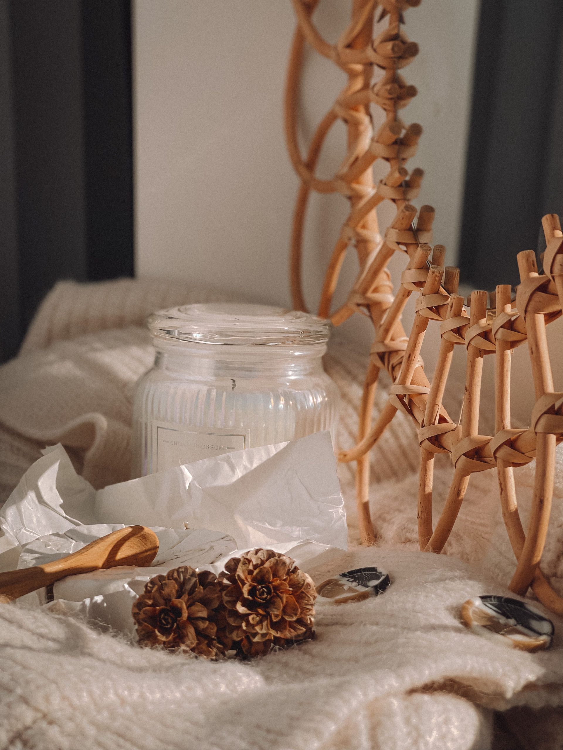 Warm and cozy winter decor featuring a glass jar candle, dried pinecones, and knitted fabric accents.