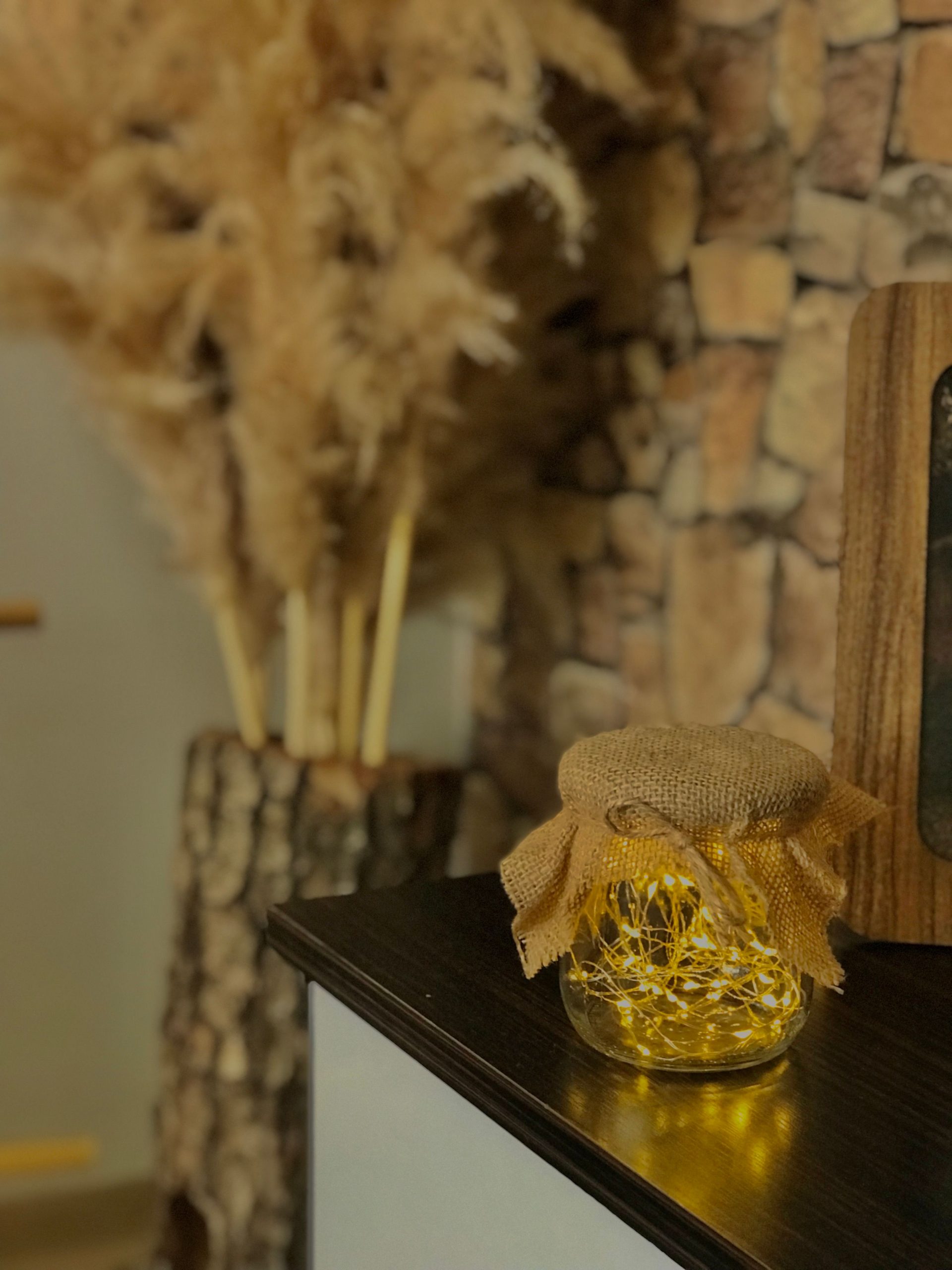 Warm and decorative indoor setting featuring a glowing jar with burlap cover, set against a stone wall and rustic elements.