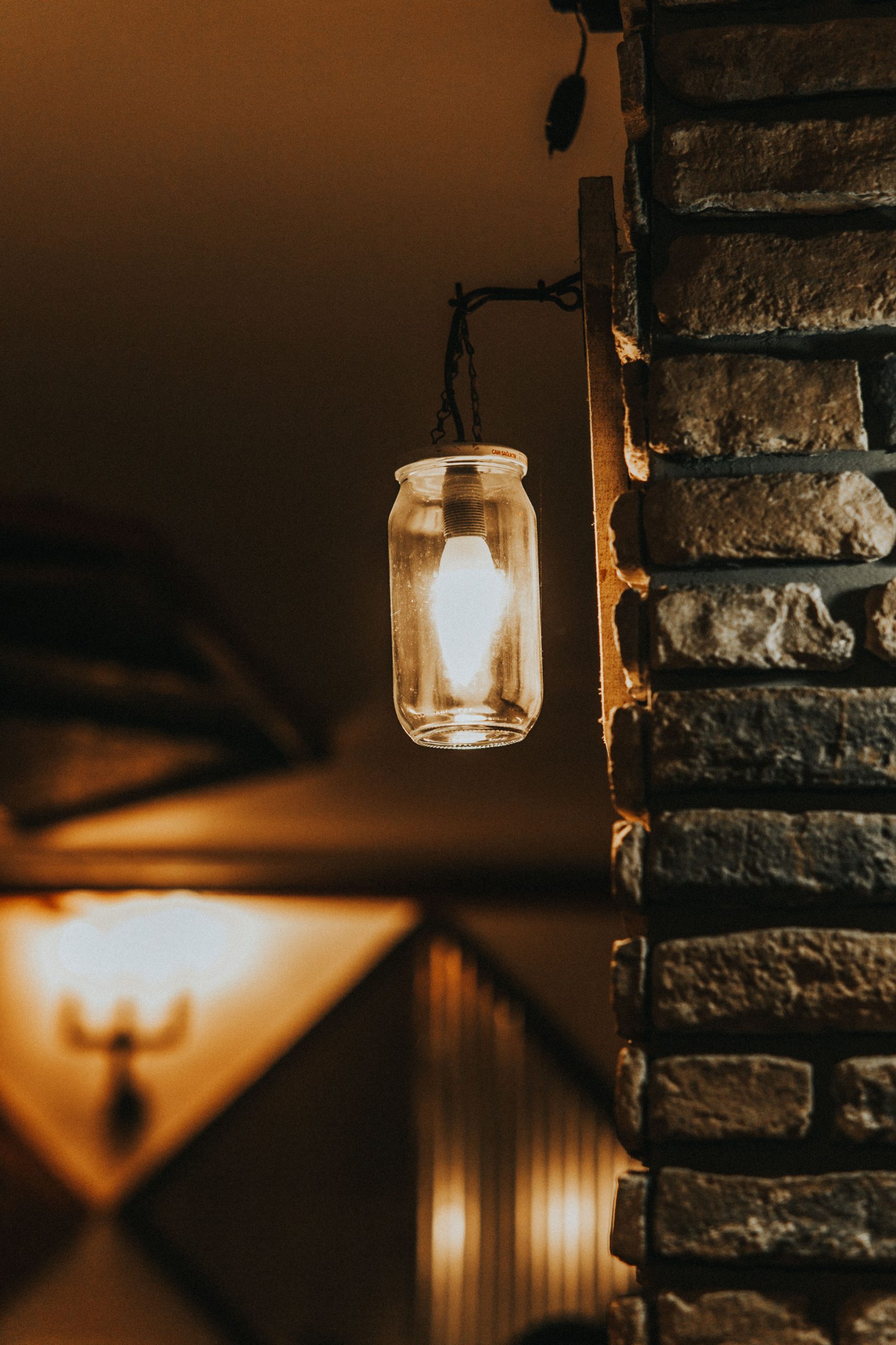 Warm light from a mason jar lamp hanging on a rustic stone wall, creating a cozy ambiance at night.
