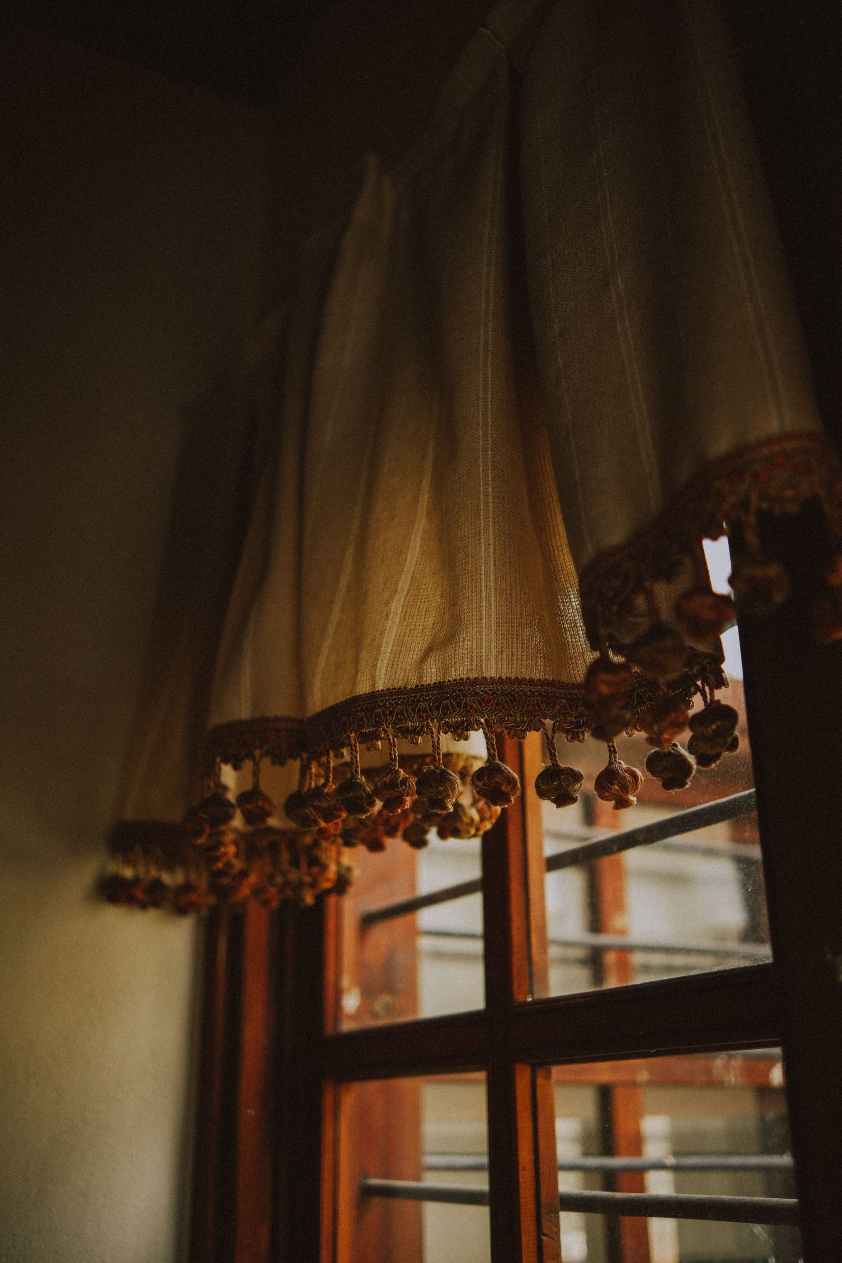 Warm sunlight filters through elegant curtains with tassels on a wooden window frame.