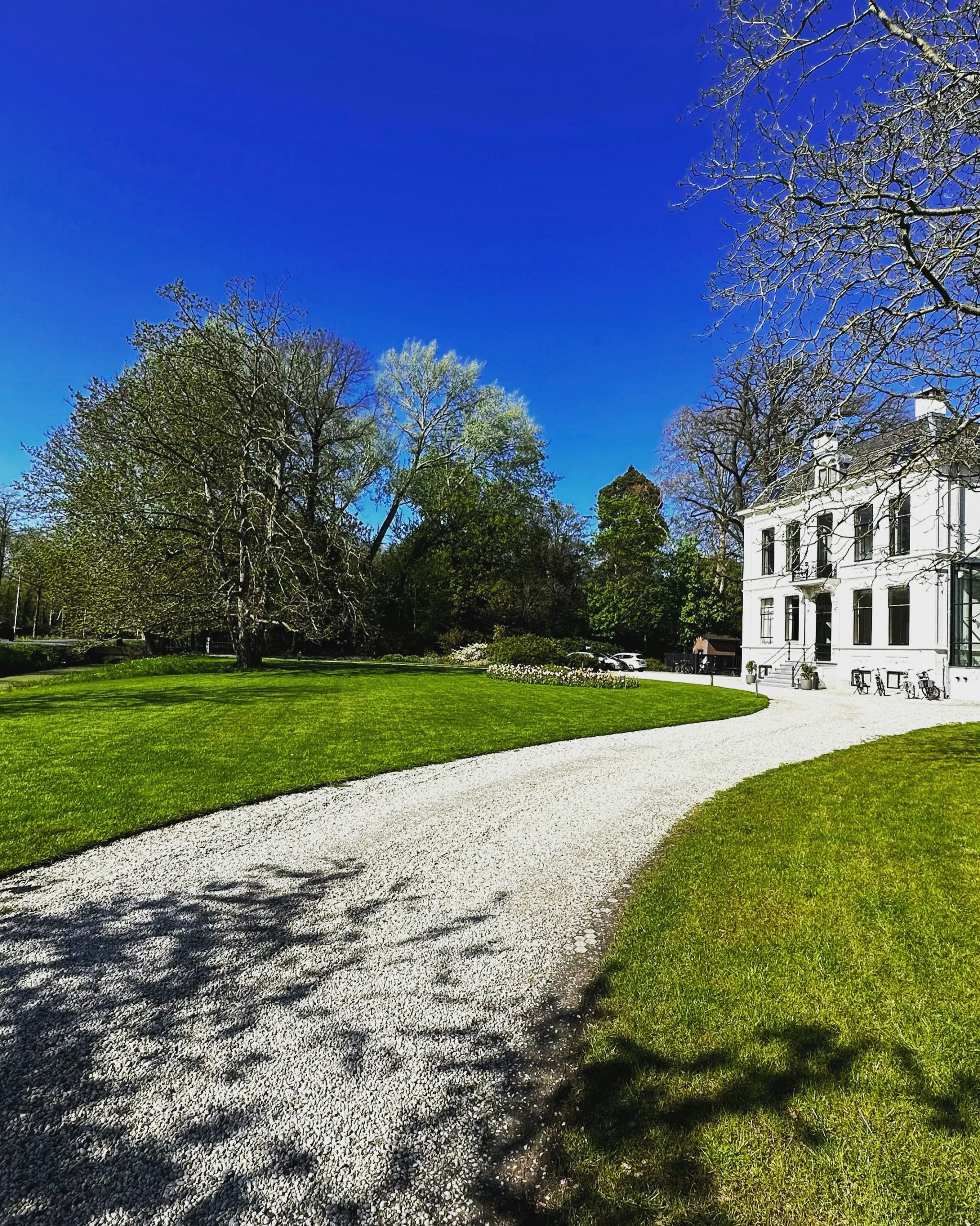 White manor house with gravel driveway and green lawn