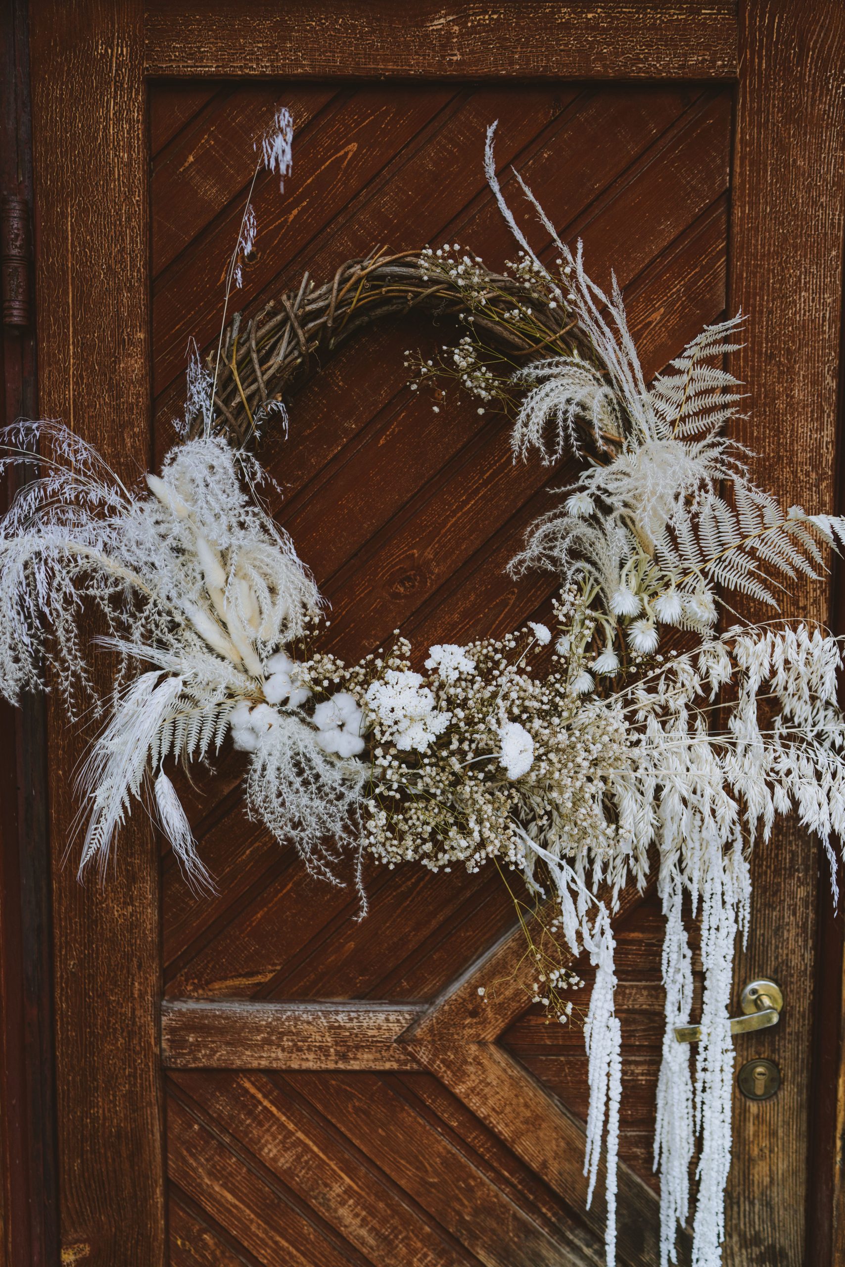 A beautiful rustic wreath hanging on a wooden door, featuring dried flowers and natural elements.