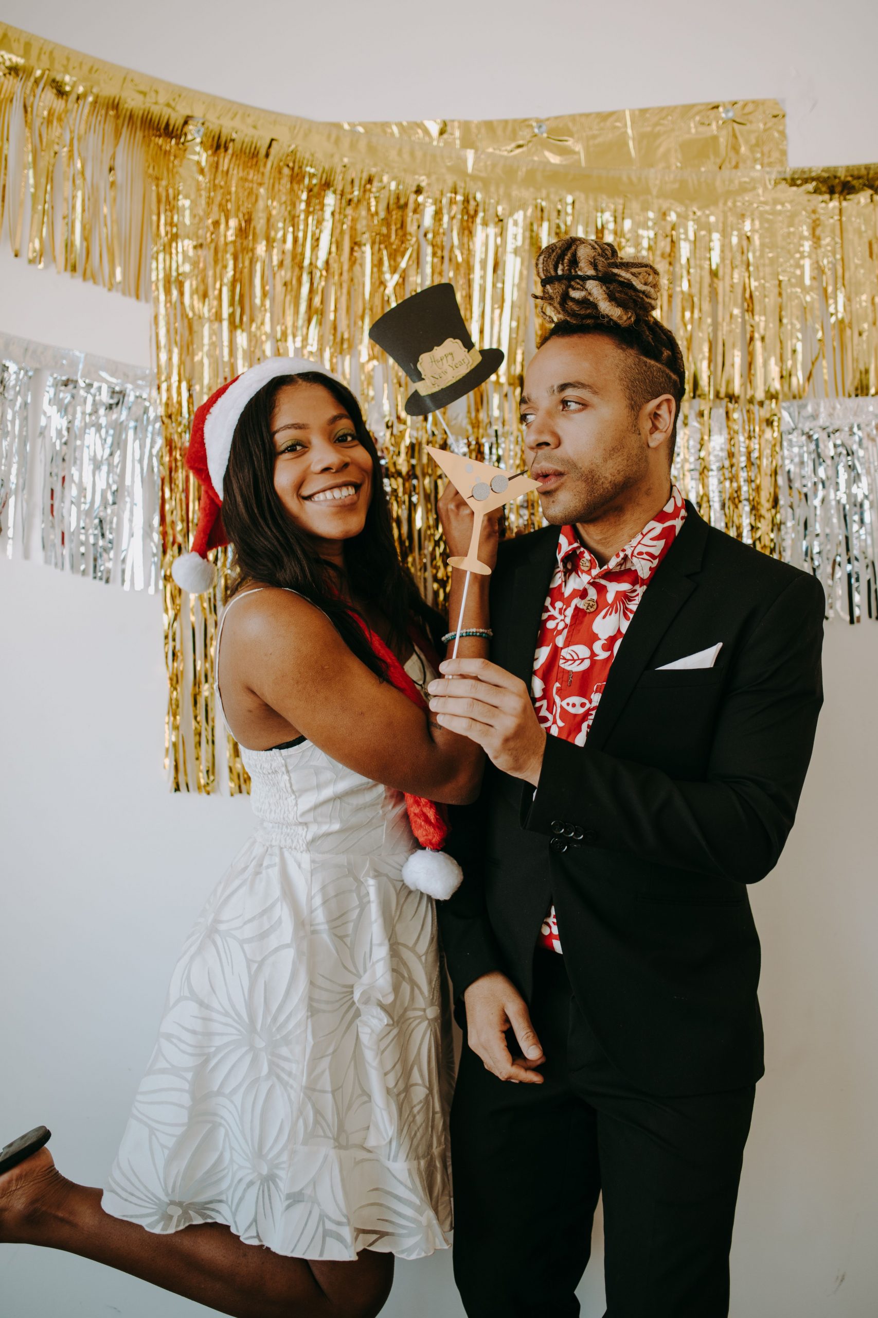 A cheerful couple celebrates a holiday party with festive decorations and props.