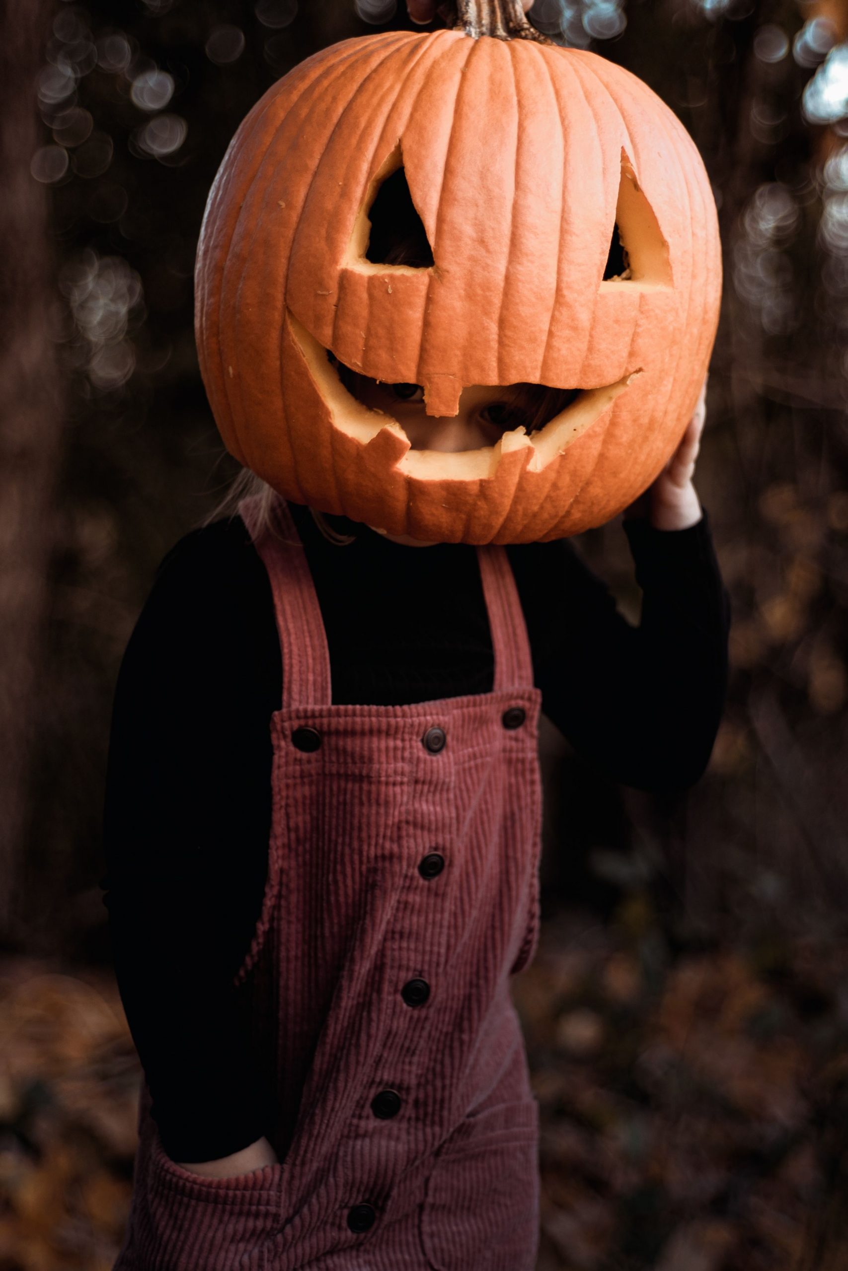 A child wearing a pumpkin on their head, celebrating Halloween outdoors in Smiths Falls, Canada.