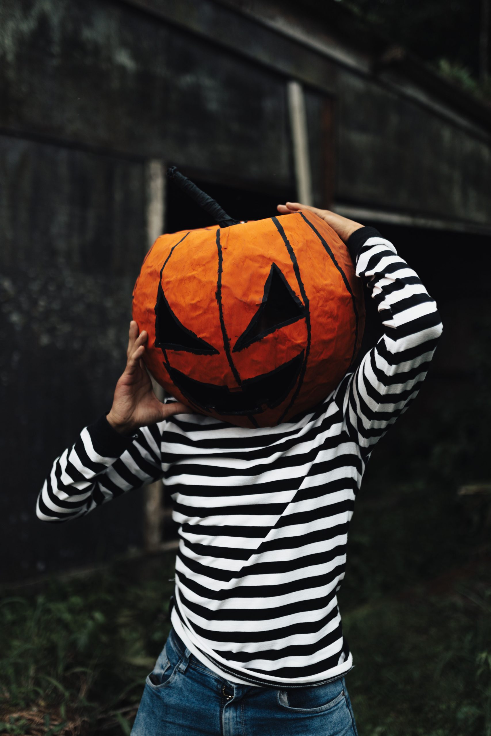 A child wearing a striped shirt and a pumpkin mask celebrates Halloween outdoors.