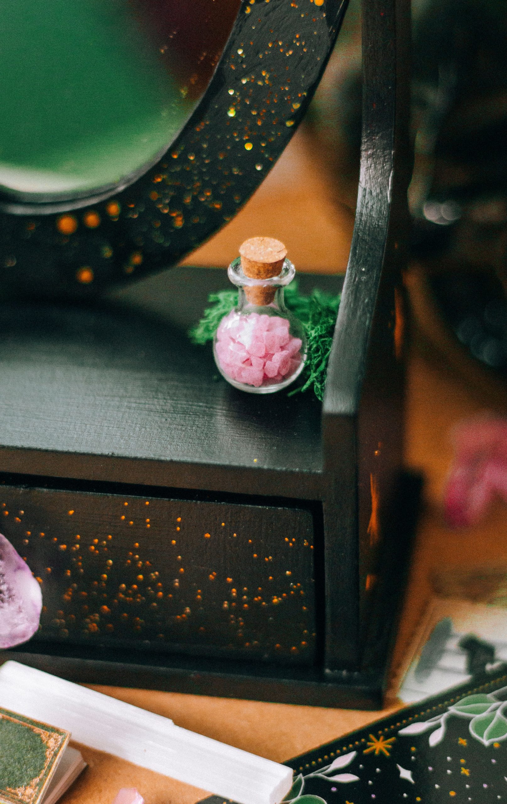 A close-up of a small corked vial with pink crystals on a decorative wooden box.