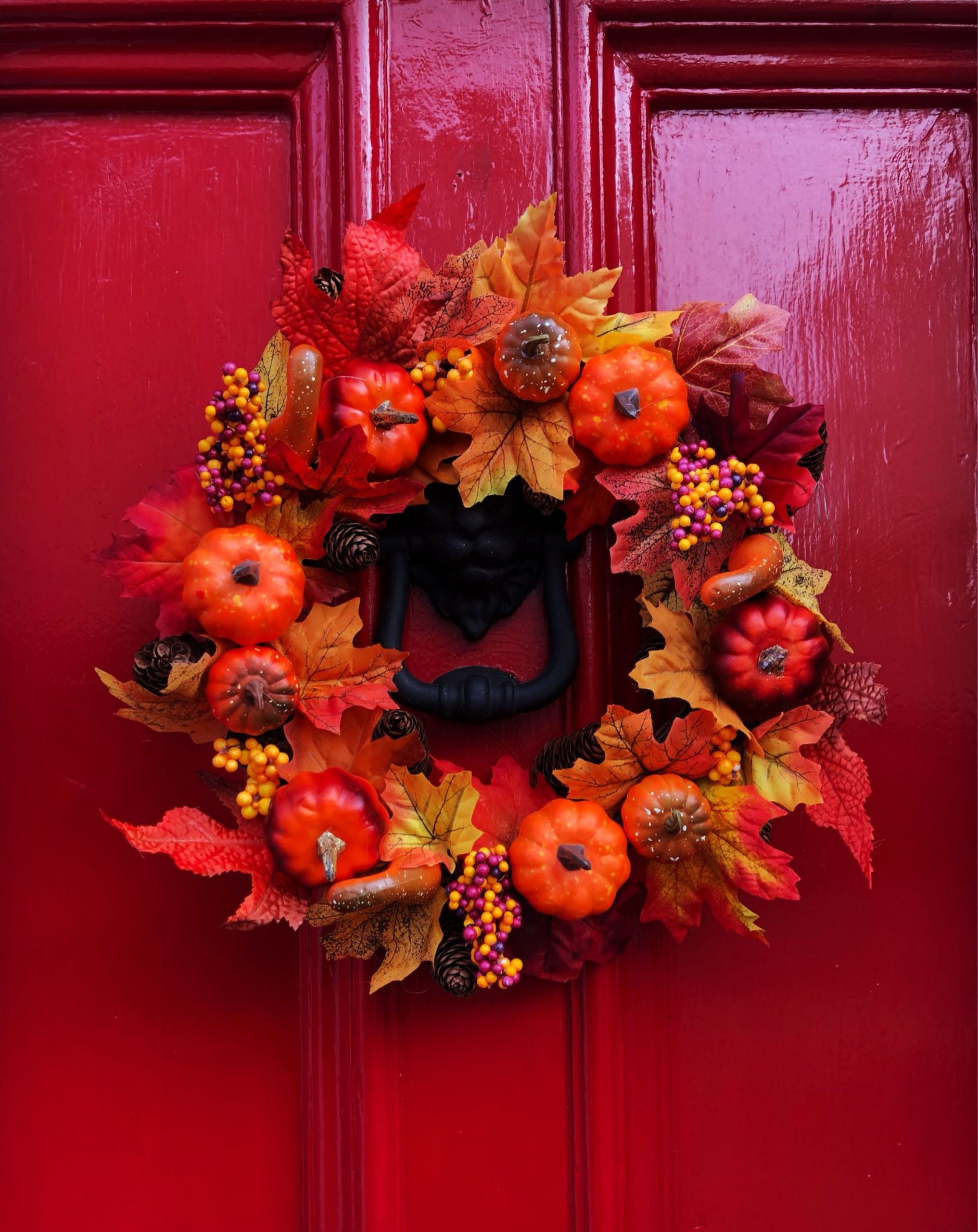 A colorful autumn flower wreath decorates a vivid red door, embodying seasonal warmth.