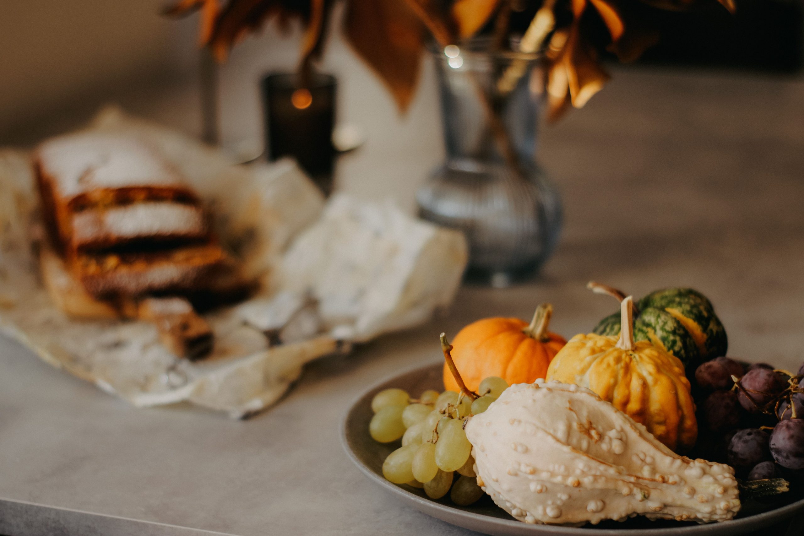 A cozy autumn arrangement with gourds, grapes, and rustic bread on a table.