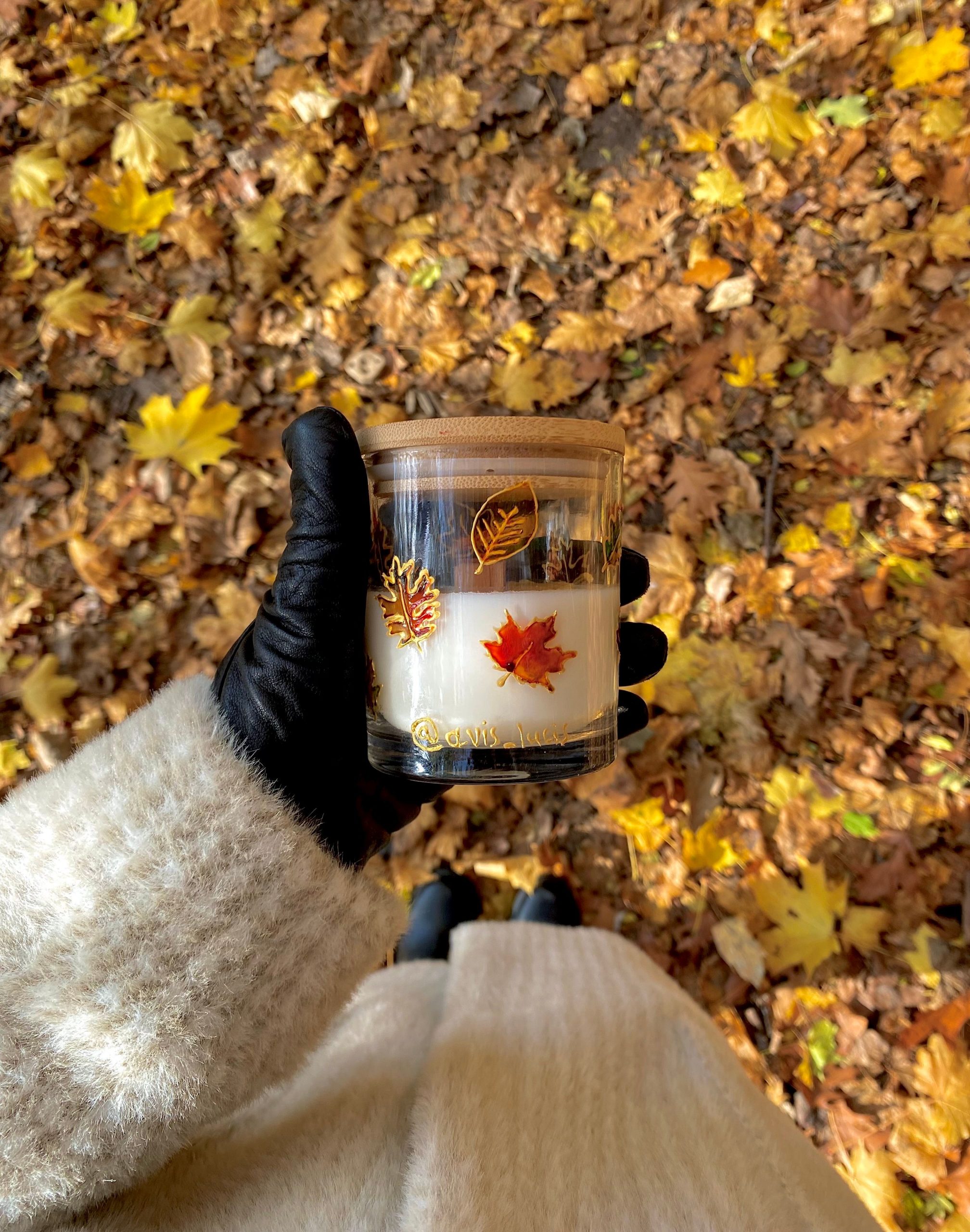 A cozy autumn scene with a candle decorated with leaves, held over a backdrop of fallen leaves.
