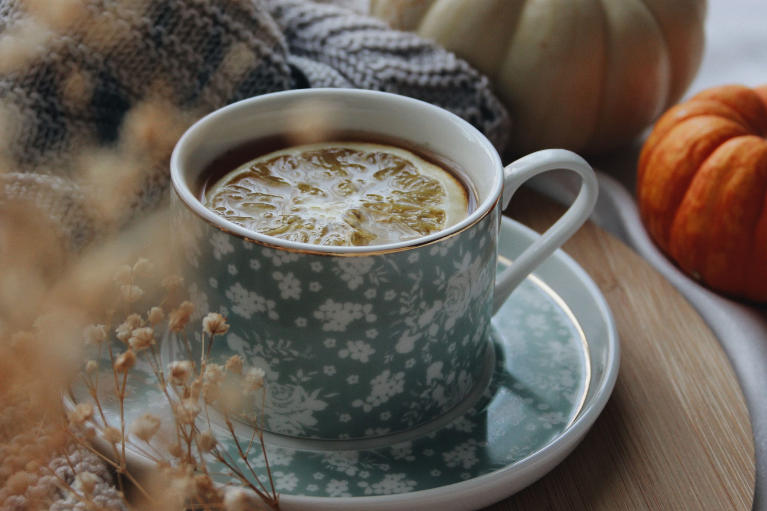 A cozy autumn scene with tea and citrus in a floral cup, surrounded by pumpkins.