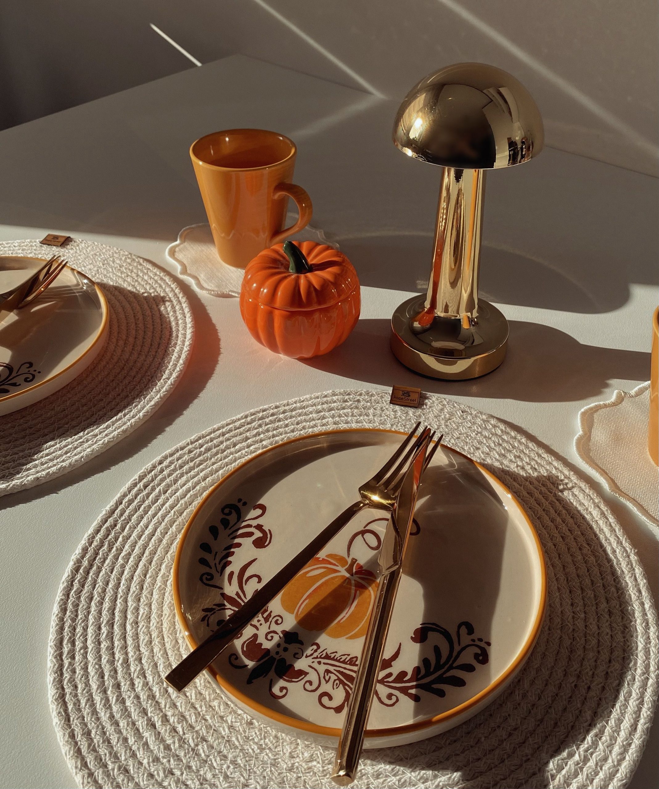 A cozy autumn table setup with pumpkin decor, golden cutlery, and warm lighting.