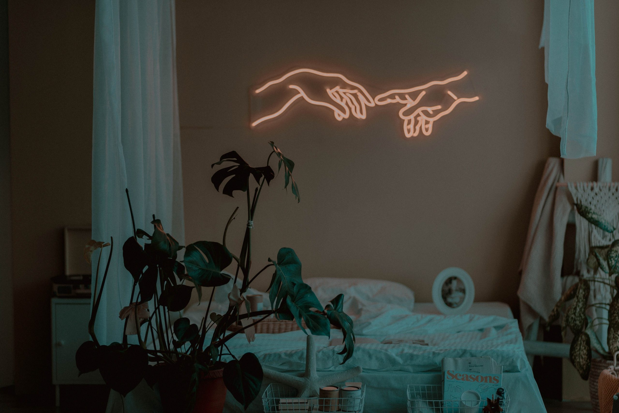 A cozy bedroom featuring neon art with indoor plants providing a calming atmosphere.