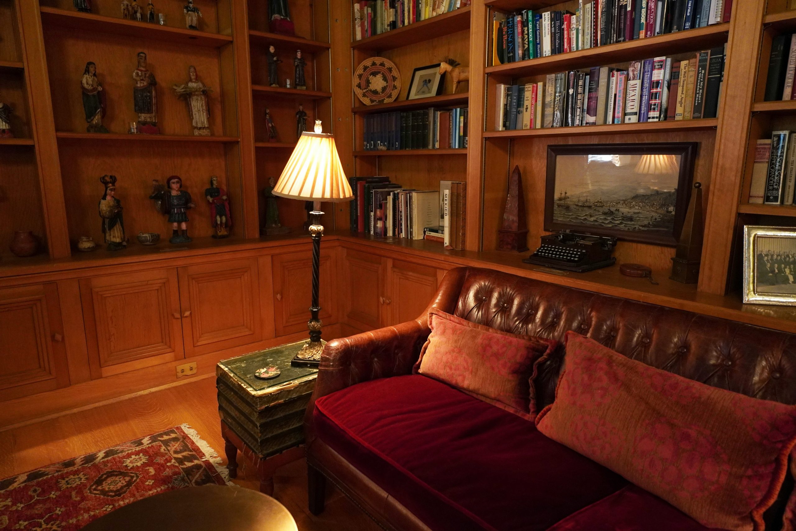 A cozy home library with rich wooden bookshelves, a vintage leather sofa, and warm ambient lighting. The elegant decor, antique typewriter, and decorative collectibles create a nostalgic and sophistic