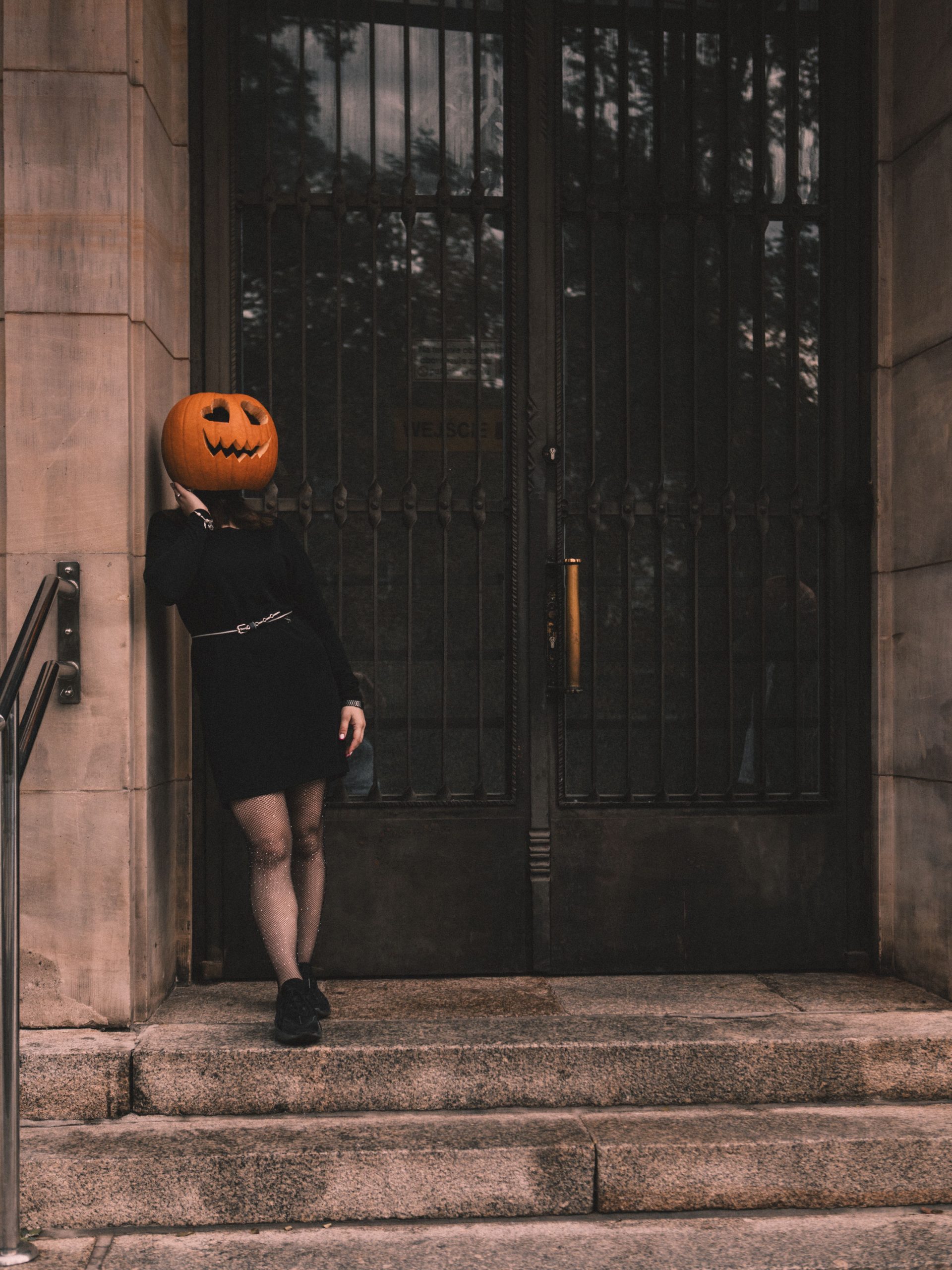 A figure with a pumpkin head leans against a gothic entrance, setting a spooky Halloween vibe.