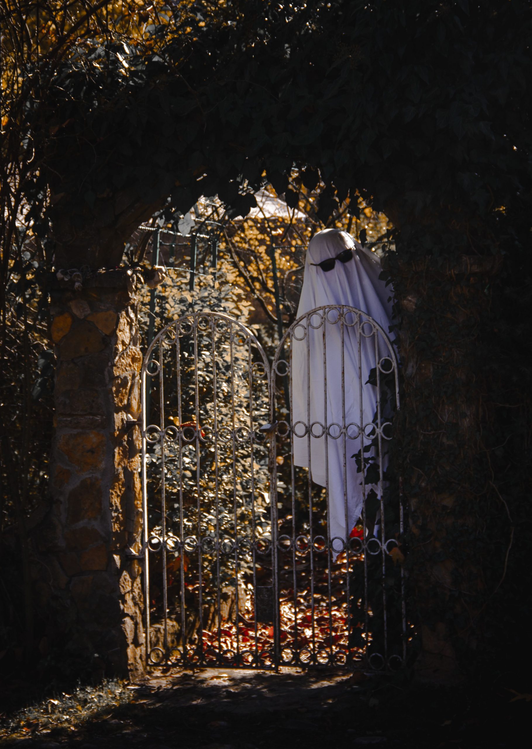 A ghostly figure stands behind an ivy-covered gate, creating a spooky Halloween atmosphere.