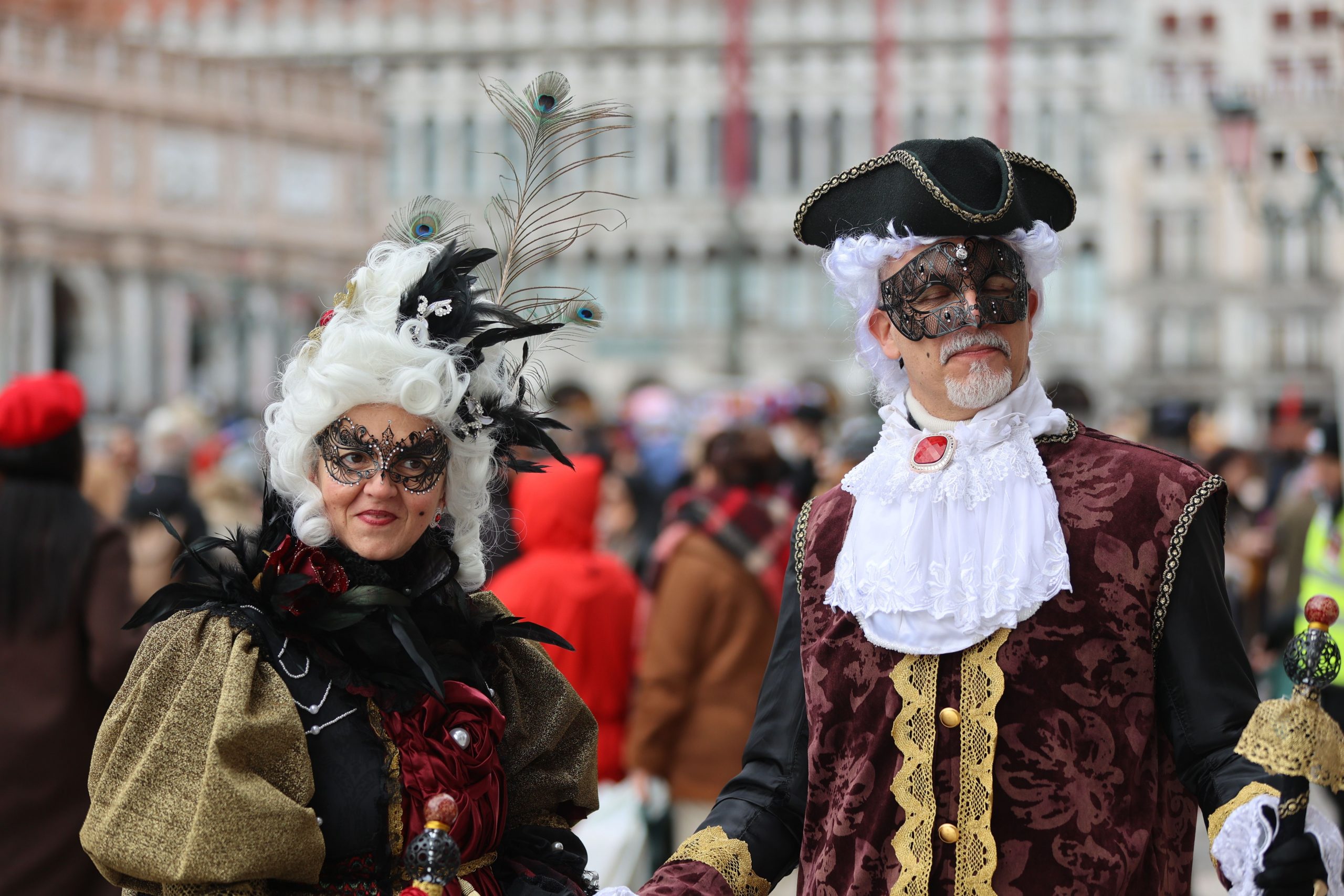A man and woman in ornate masquerade costumes at a vibrant street festival.