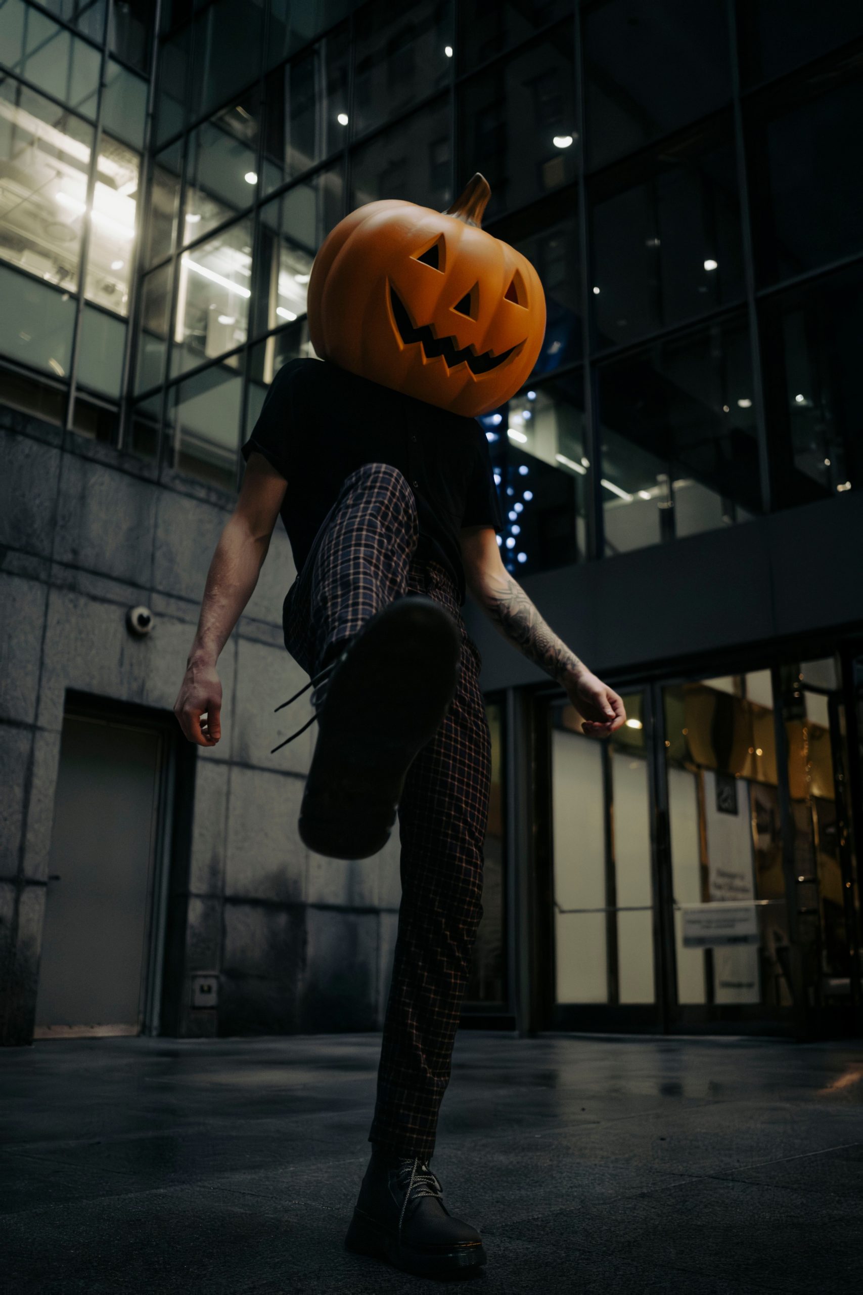 A man with a carved pumpkin head strolls through a modern urban area in Chicago at night.